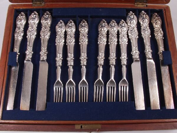 Set of twelve pairs of white metal tea knives and: Set of twelve pairs of white metal tea knives and forks, with scroll cast terminals, contained in a fitted wooden case. (Apparently unmarked.)