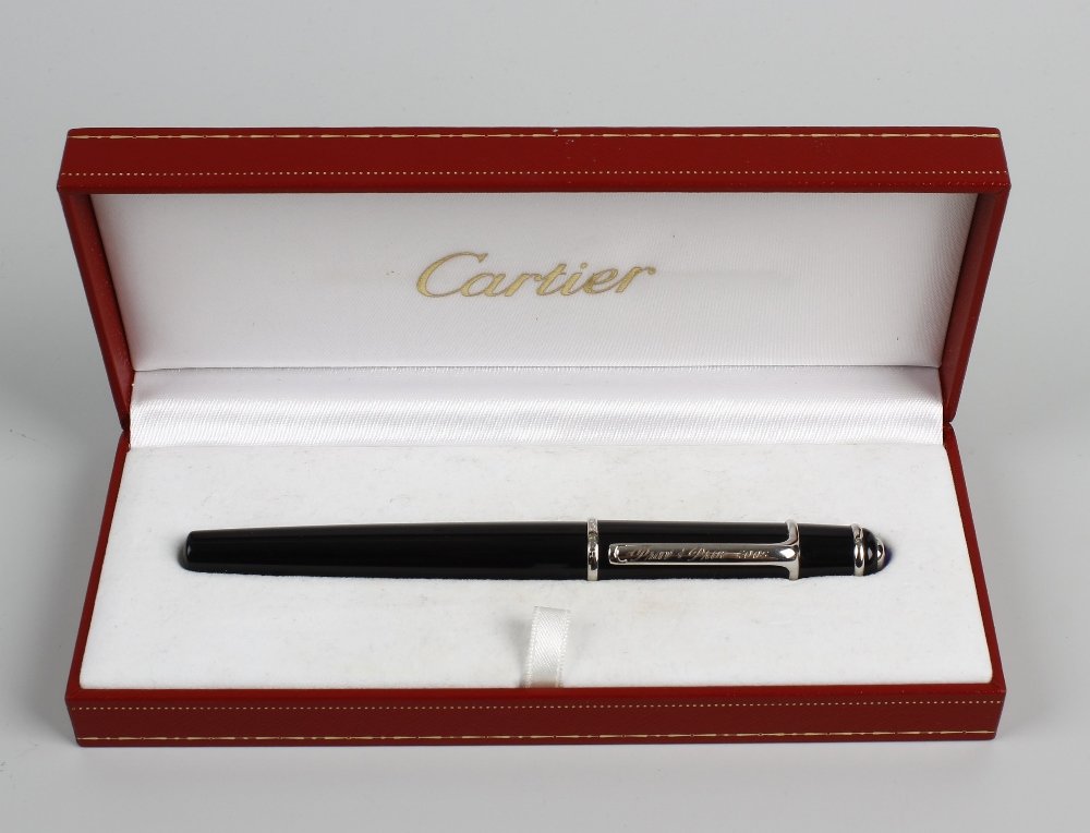 A Cartier ball point pen.: A Cartier ball point pen. The black resin body having silvered banding and clip with personal engraving leading to a blue gem inset terminal, 5.5" (14 cm) long, in fitted maker's box.
