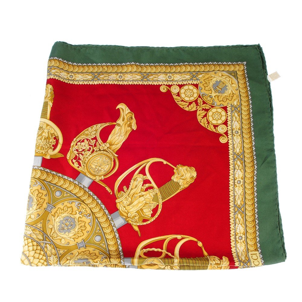 GUCCI - a silk scarf.: GUCCI - a silk scarf. The gold coloured patterned shield to the centre surrounded by decorative sword hilts, with a red background and green and gold border. Measuring 85 by 85cms.