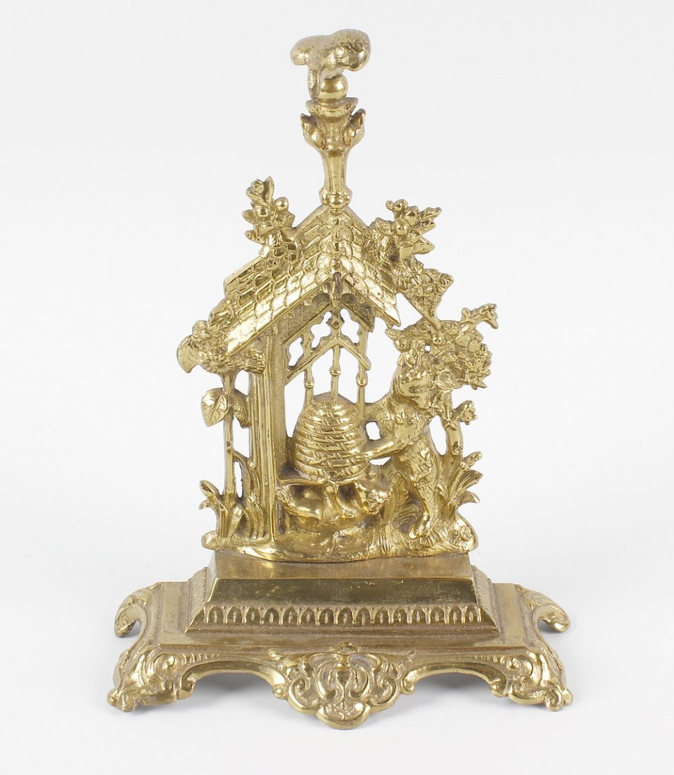 A Victorian brass pocket watch stand, modelled as two: A Victorian brass pocket watch stand, modelled as two bears holding a honey pot beside sunflowers and below a pitched roof, the whole raised upon a stepped and scrolled base, 9 (23cm) high. With knock