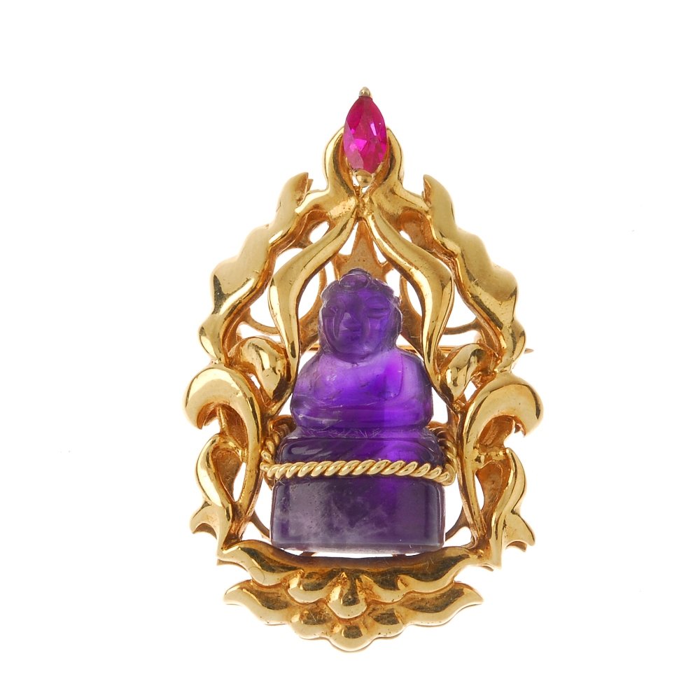 An amethyst buddha brooch. The carved amethyst Buddha,: An amethyst buddha brooch. The carved amethyst Buddha, within a marquise red paste highlight stylised scroll surround. Length 3.8cms. Weight 13.1gms. Overall condition good. Minor surface scratches/we