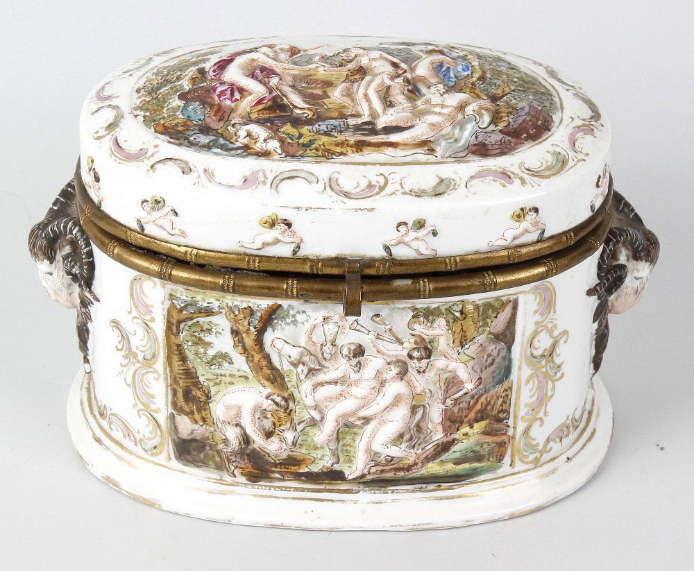 A Capodimonte porcelain box, of oval form with hinged: A Capodimonte porcelain box, of oval form with hinged cover, decorated with three raised painted panels depicting nude classical figures, with two raised rams heads to sides, mark to base, 5.5 (14cm).