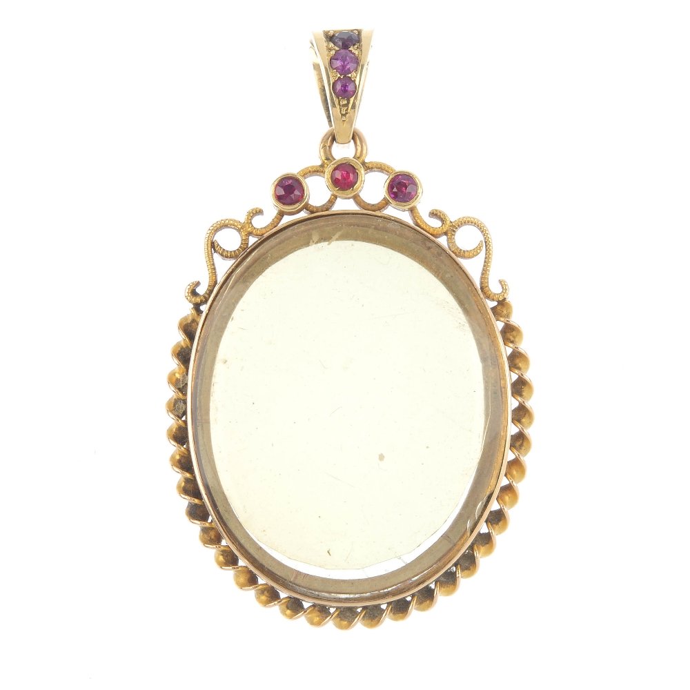 A ruby photograph locket. Of oval-shape outline, the: A ruby photograph locket. Of oval-shape outline, the vacant hinged centre panel, within a twist surround, to the circular-shape ruby collet scrolls and similarly-set tapered surmount. Length 5.2cms. W