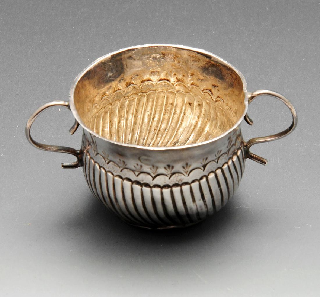 A George I toy or miniature Britannia silver porringer,: A George I toy or miniature Britannia silver porringer, the circular fluted form with twin scroll handles raised upon a stepped base, hallmarked London 1721, maker's mark partly distorted possibly Jam