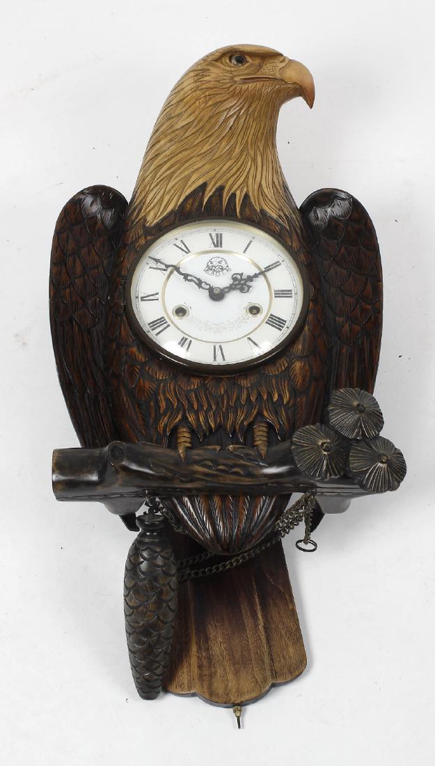 An unusual carved eagle wall clock, the 6-inch Roman: An unusual carved eagle wall clock, the 6-inch Roman dial with eagle motif and banner beneath XII, the two-train movement operating via the bird's tail as pendulum, in a two-tone carved case modelled