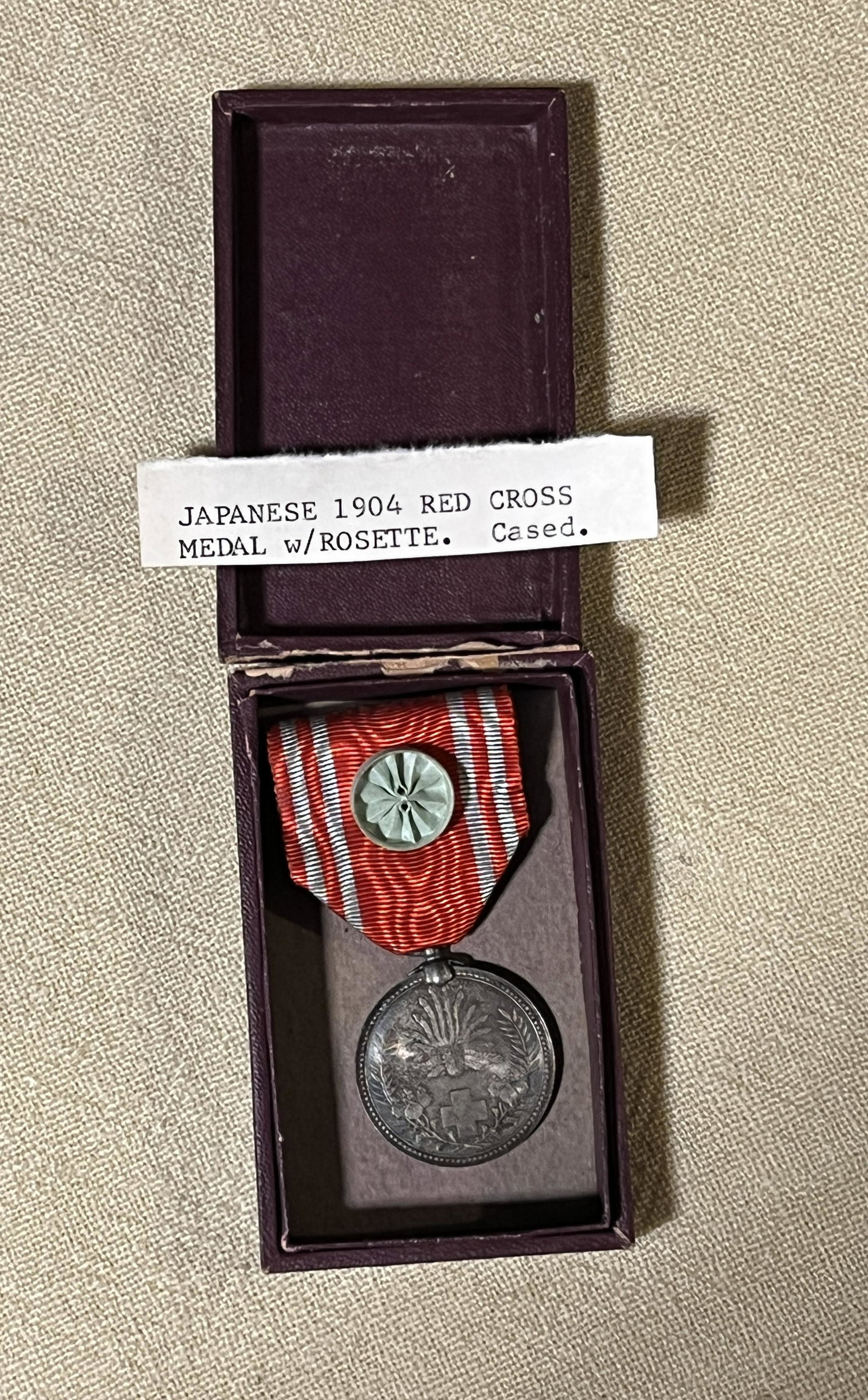 CASED 1904 JAPANESE RED CROS MEDAL W/ROSETTE: CASED 1904 JAPANESE RED CROS MEDAL W/ROSETTE. COMES IN THE ORIGINAL BOX. IN MINT OVERALL SHAPE AND CONDITION WITH A BEAUTIFUL OVERALL PATINA. A GREAT FIND AND AN EXCELLENT ADDITION TO YOUR COLLECTION.
