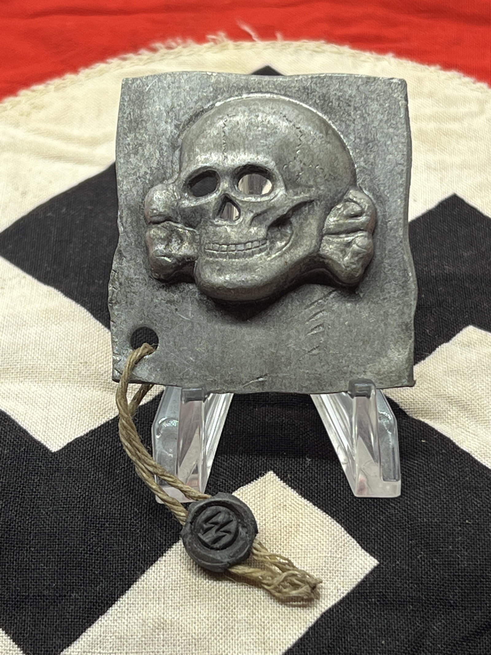 WW2 GERMAN TOTENKOPF SS SKULL BADGE W/SS TAG: WW2 GERMAN TOTENKOPF SS SKULL BADGE W/SS TAG. A VERY RARE FIND. IT IS IN MINT OVERALL SHAPE AND CONDITION WITH A BEAUTIFUL OVERALL PATINA. A GREAT FIND AND AN EXCELLENT ADDITION TO YOUR COLLECTION.