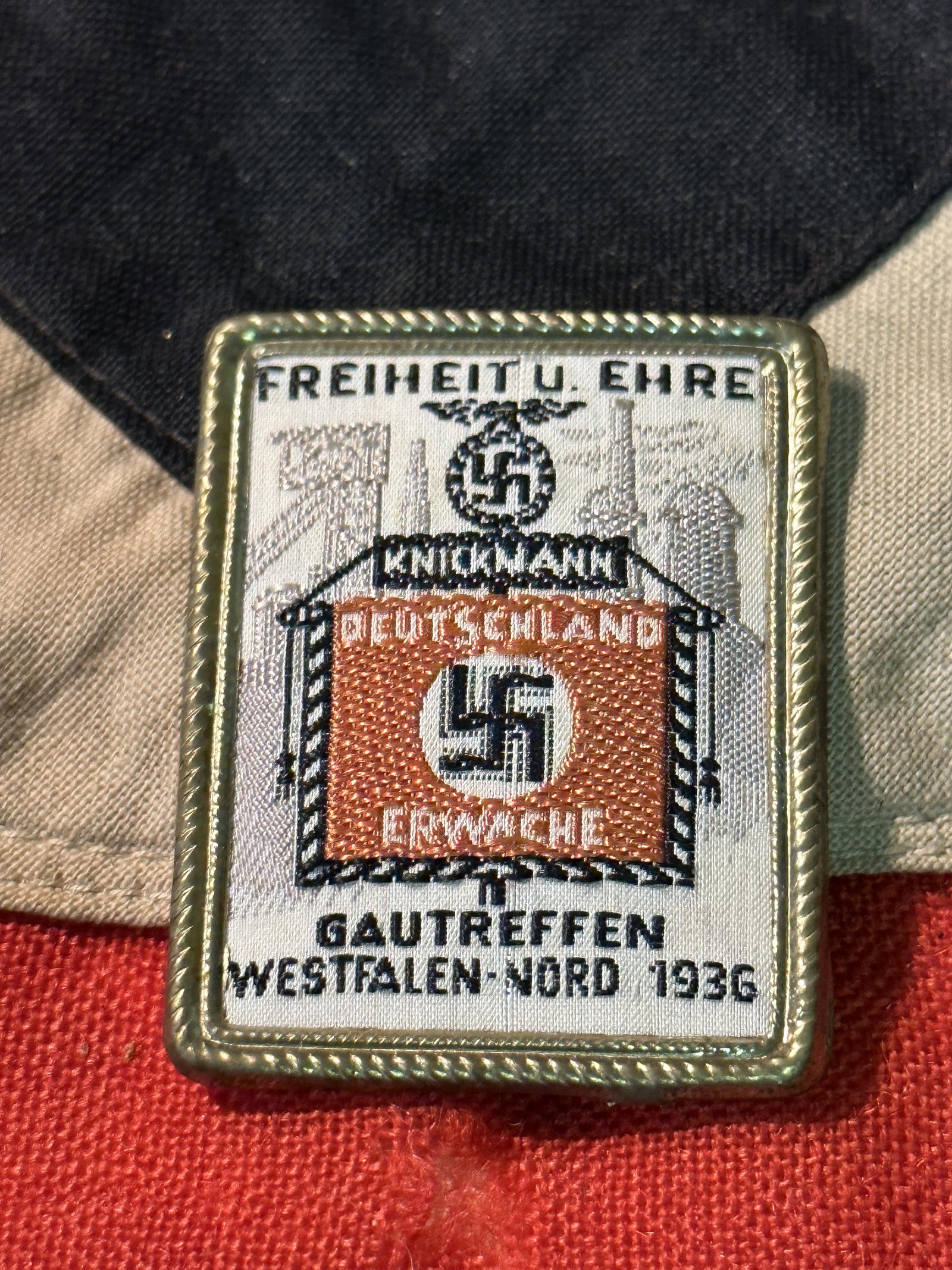 WW2 GERMAN DEUTSCHLAND ERWACHE TINNIE BADGE WITH MAKER MARKS: WW2 GERMAN DEUTSCHLAND ERWACHE TINNIE BADGE WITH MAKER MARKS. Cloth front. Gau Day Badge 1936 - The badge reads "Freiheit u. Ehre Gautreffen Westfalen Nord 1936" ( Freedom and Honor Gau Meeting Westph