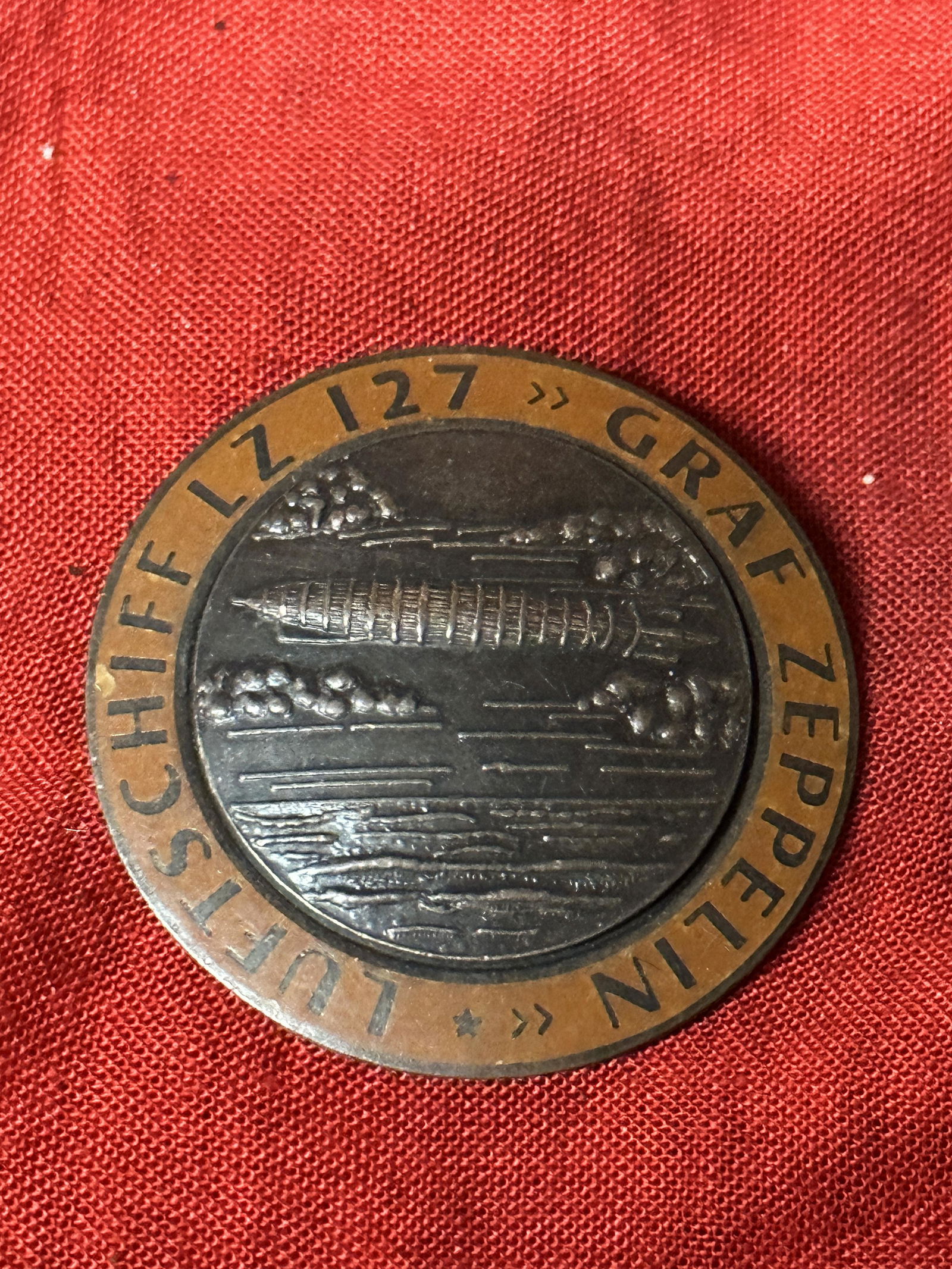RARE WW2 GERMAN GRAF ZEPPELIN LZ 127 AIR SHIP BADGE IN ORANGE BY FLL: RARE WW2 GERMAN GRAF ZEPPELIN LZ 127 AIR SHIP BADGE IN ORANGE BY FLL. A RARE FIND WITH THE MAKER MARKS FLL ON THE REVERSE. SHOWS GOOD WEAR AND USE WITH A BEAUTIFUL PATINA THROUGHOUT. PLEASE VIEW ALL D