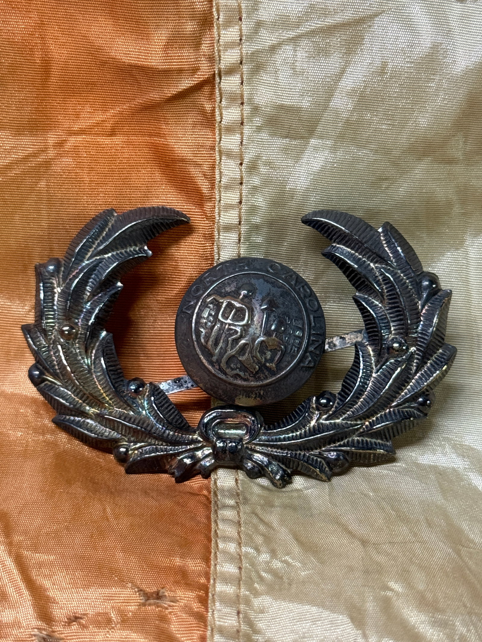 CSA CIVIL WAR CONFEDERATE NORTH CAROLINA WITH WREATH BADGE INSIGNIA: SCARCE CIVIL WAR CONFEDERATE NORTH CAROLINA WITH WREATH BADGE INSIGNIA. A RARE FIND. SHOWS GOOD WEAR AND USE WITH A BEAUTIFUL PATINA THROUGHOUT. LOOKS STUNNING WITH DETAILED CRAFTSMANSHIP. PLEASE VIEW