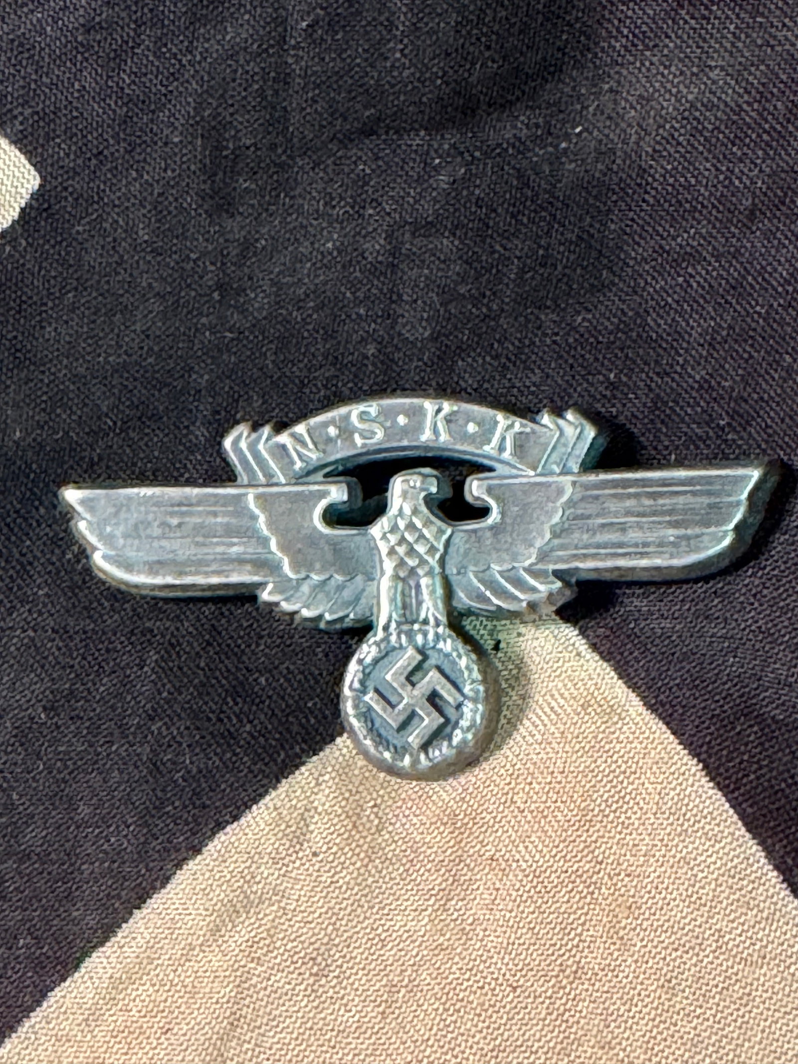 WWII NSKK, 2nd Model Crash Helmet Emblem: WWII NSKK, 2nd Model Crash Helmet Emblem. Bright aluminum eagle with the letters NSKK in a banner above the eagles head. All of the three aluminum attaching prongs are on the reverse.