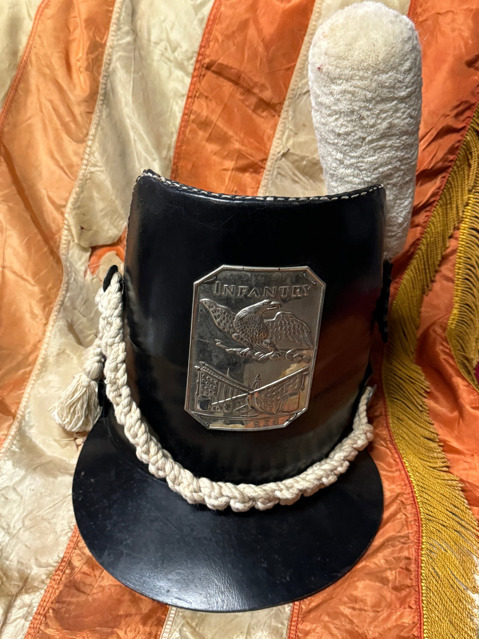 US WAR OF 1812 INFANTRY ENLISTED SHAKO HAT CAP: US WAR OF 1812 INFANTRY ENLISTED SHAKO HAT CAP. ombstone style front, leather body, with a pressed metal front plate, black leather rosette on the left side, and white cord trim. A rare find. Shows go