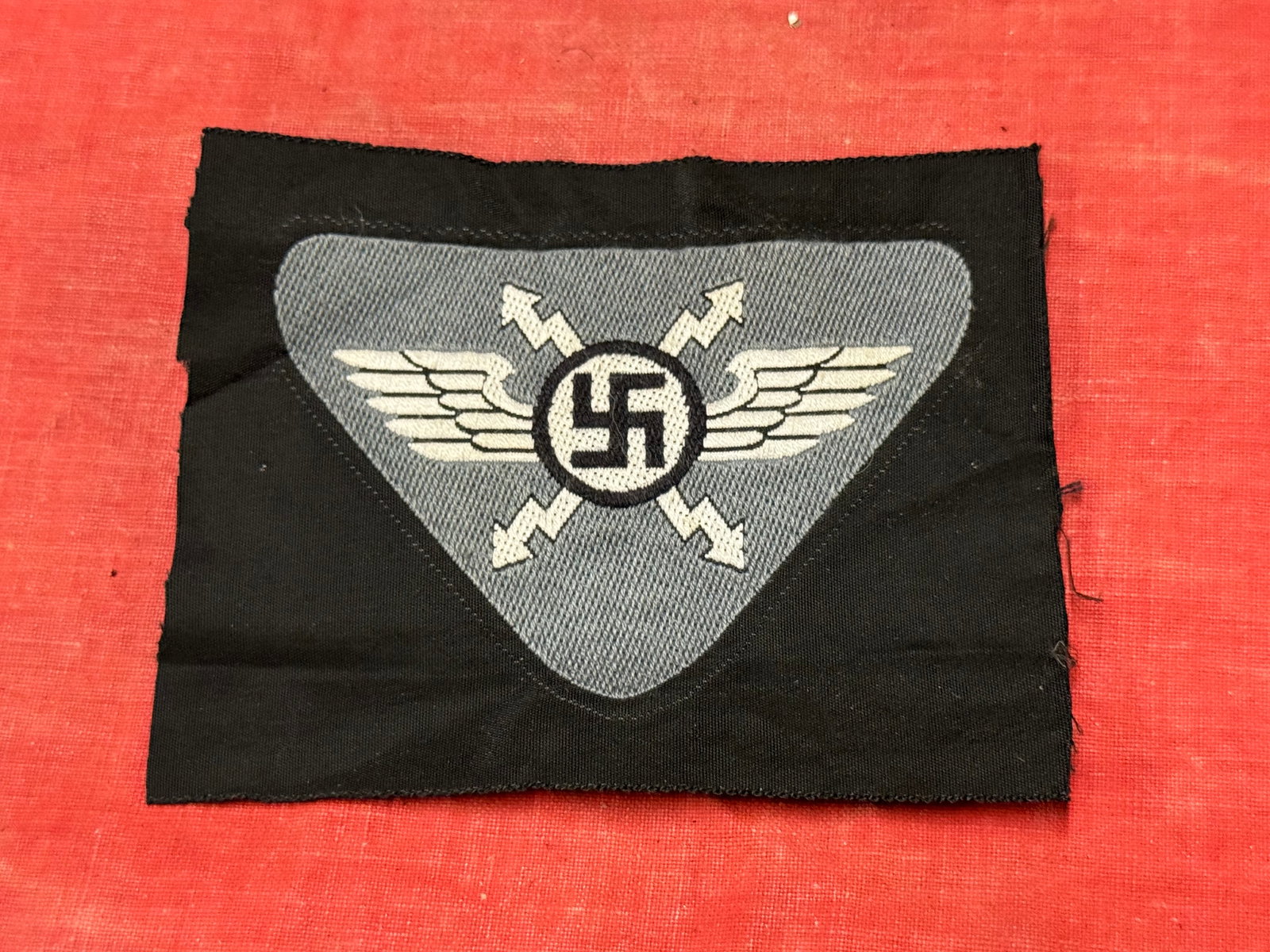WW2 German Third Reich National Socialist Flyers Corps (NSFK) Insignia: WW2 German Third Reich National Socialist Flyers Corps (NSFK) Insignia. Made of BeVo woven construction. The patch depicts a swastika in the center with a pair of lightning bolts and wings in white on