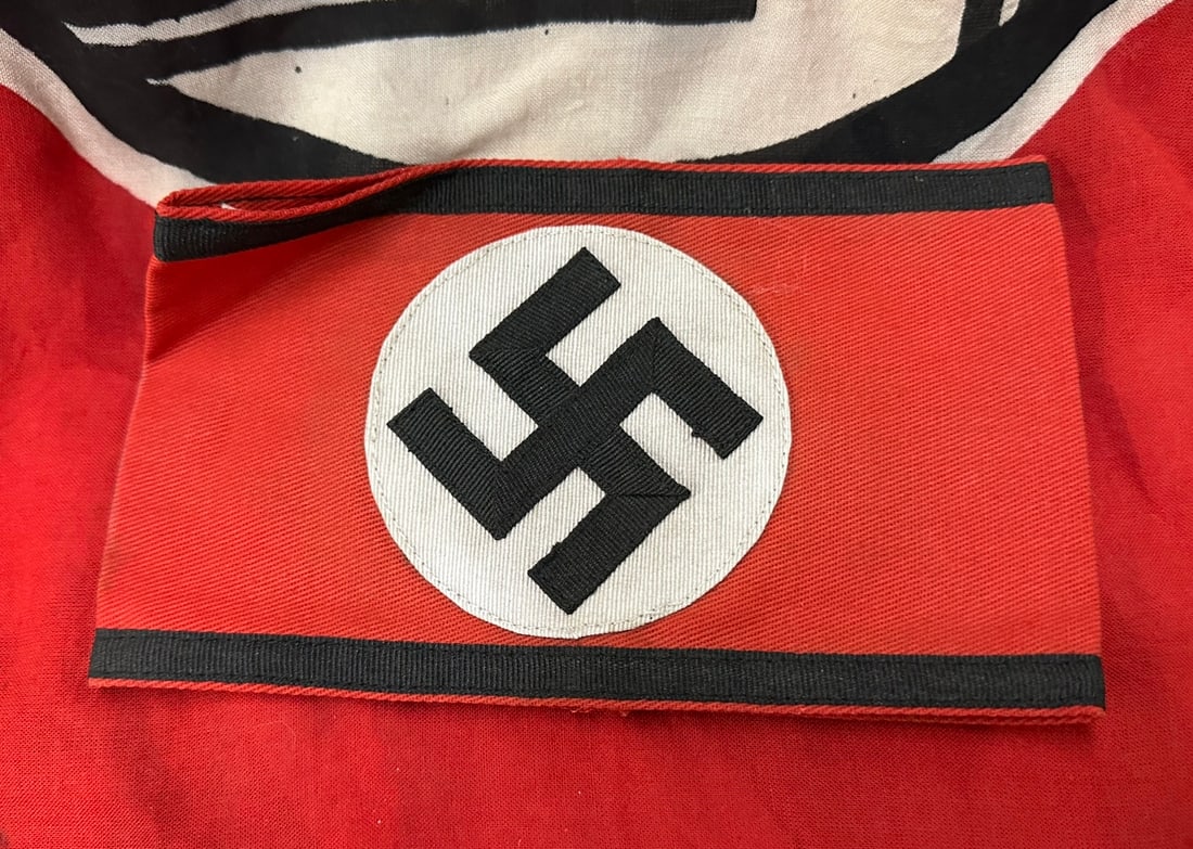 WW2 GERMAN ALLGEMEINE SS ARMBAND WITH RZM PAPER TAG: WW2 GERMAN ALLGEMEINE SS ARMBAND WITH RZM PAPER TAG. An early SS Armband, constructed in red cotton with a machine-embroidered disc measuring 85mm, with a black canted swastika stitched on. The top an