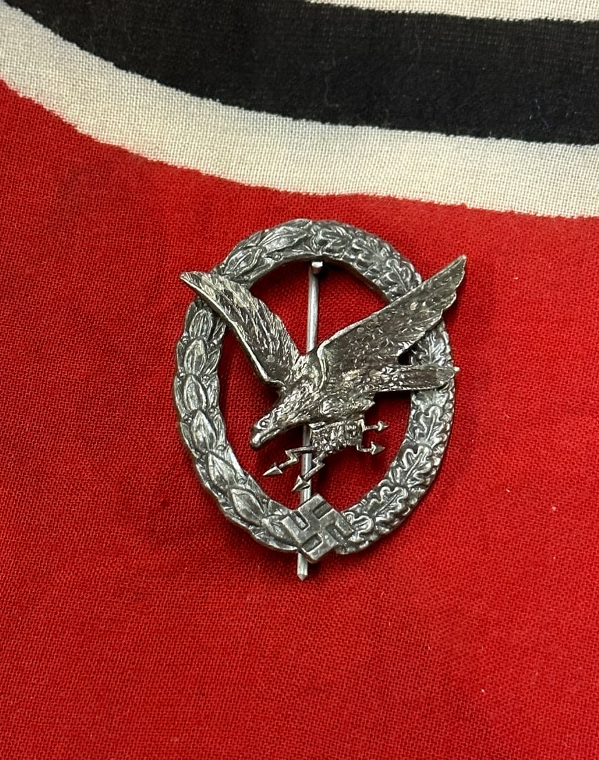 WW2 German Luftwaffe radio operator air gunner badge: WW2 German Luftwaffe radio operator air gunner badge. Early full nickel silver ‘Fliegerschützen’ with produced parts and IMME makers mark on the back of the eagle. Remains in lightly worn conditi