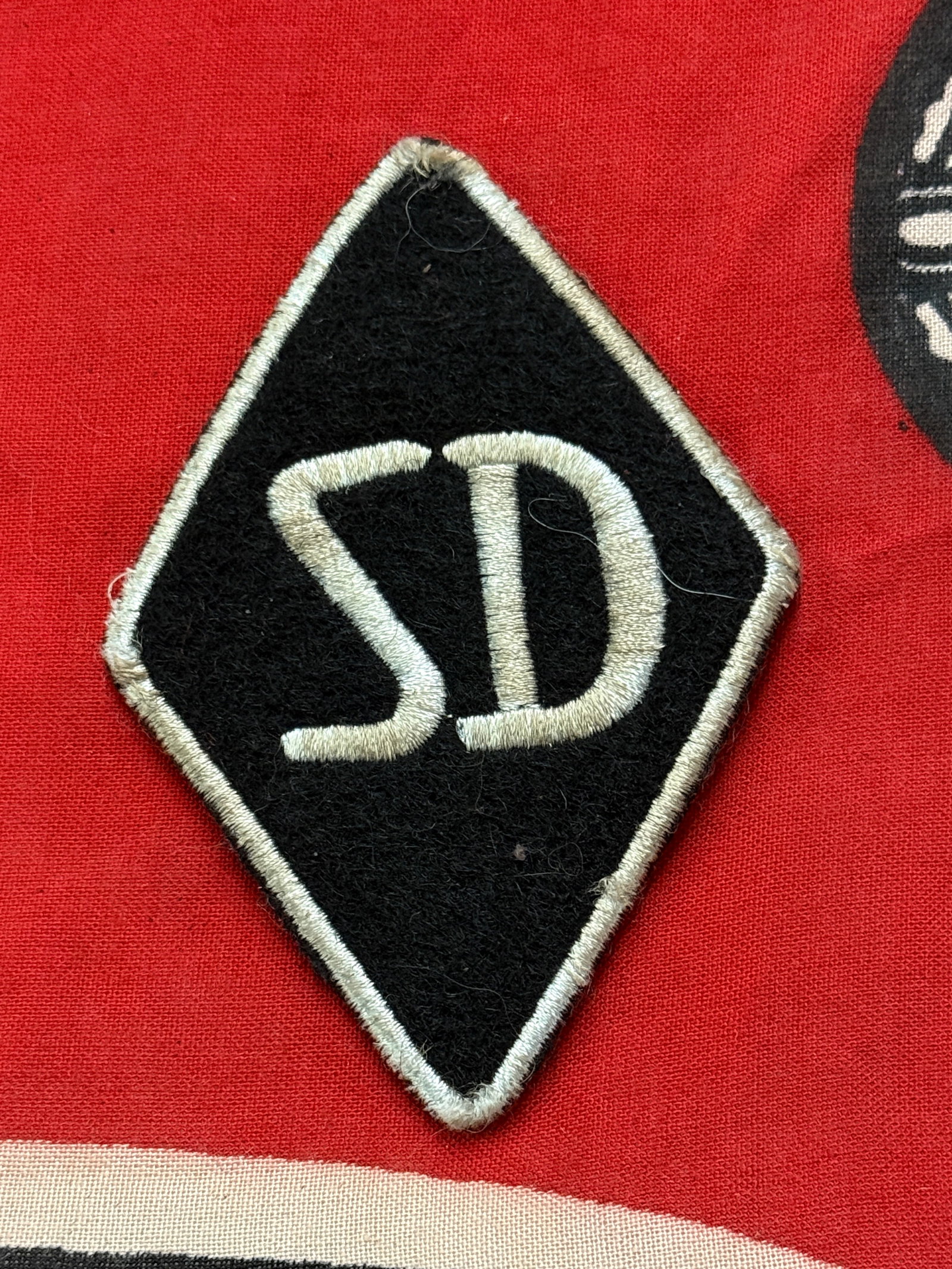 WW2 German An Ss – Sd Officer’s Sleeve Diamond Insignia: WW2 German An Ss – Sd Officer’s Sleeve Diamond Insignia. Constructed of flat silver wire on top of black wool diamond shaped base, and edged in silver twisted wire. "SD" indicates “ Sicherheits 