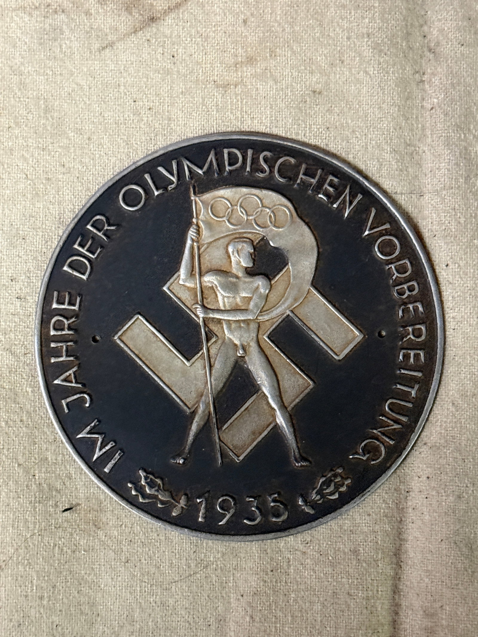 Germany, Third Reich. A 1935 Olympic Games Preparation Commemorative Table Medal SKU:: (Olympische Sommerspiele Erinnerungsmedaille). Constructed of blackened magnetic iron, the obverse bearing a central raised mobile swastika overlaid by an Olympic flag bearer, circumscribed by a raise