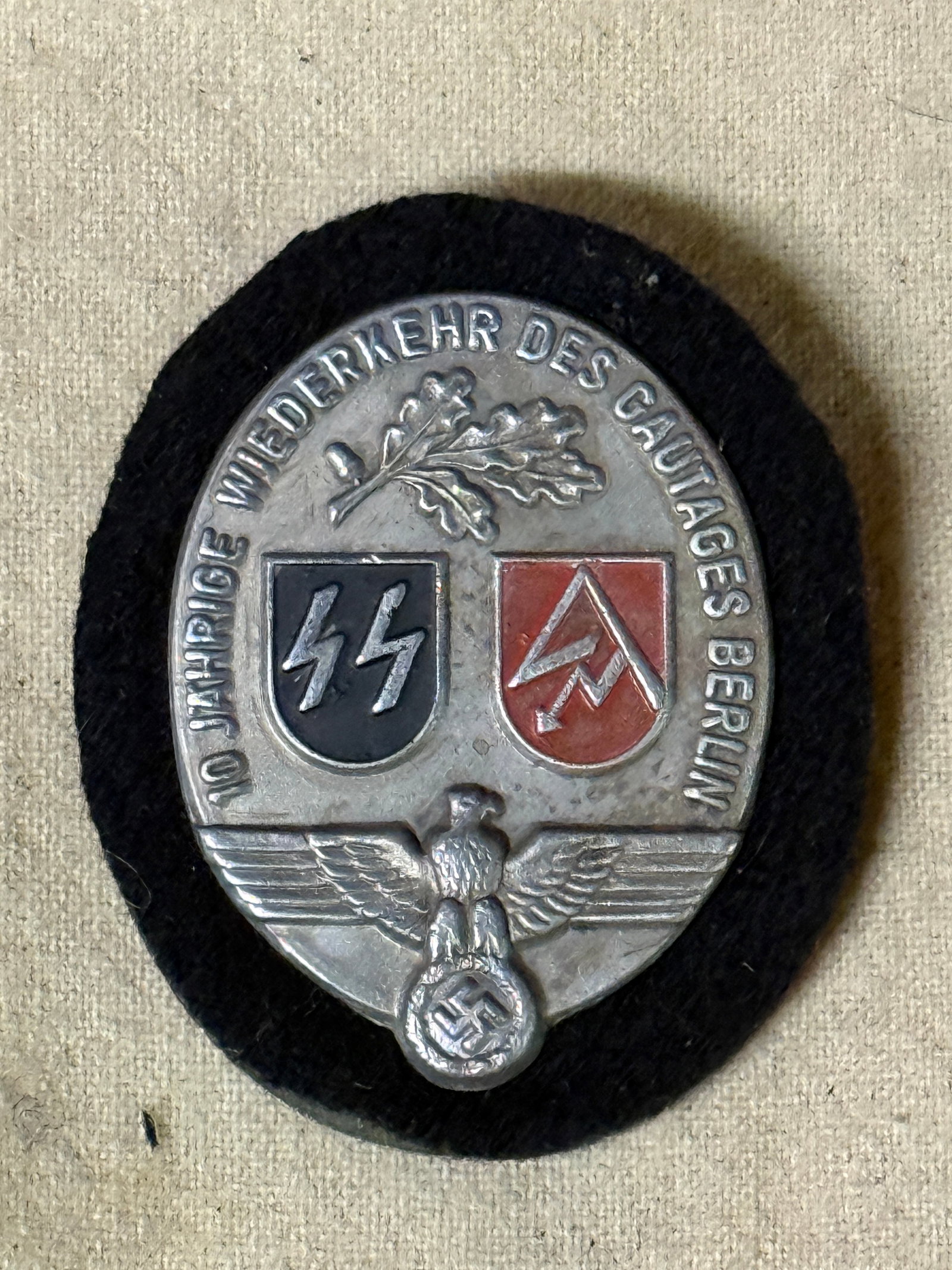 WW2 German SS SA 10 Year Rally Tinnie With Maker Marks: WW2 German SS SA 10 Year Rally Tinnie With Maker Marks. Pressed aluminium badge mounted onto black wool with back plate and pin. Overall measurement; H=55mm x W=45mm.