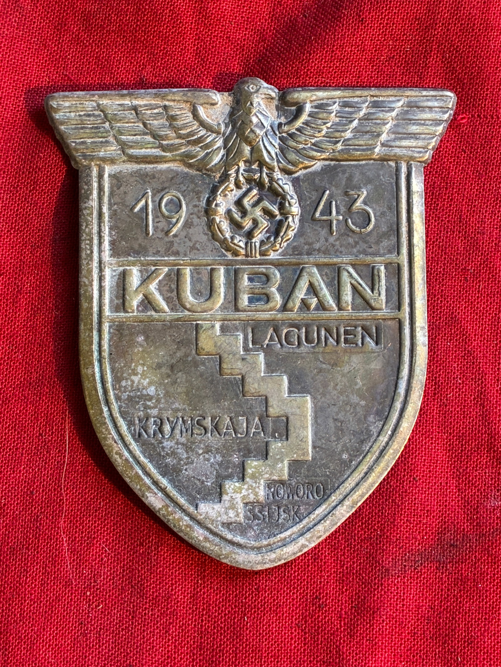 German WWII Kuban Bridgehead Shield Decoration - Armelschild Kuban: German WWII Kuban Bridgehead Shield Decoration - Armelschild Kuban. This is a very good example with an excellent metal shield unattached to a wool uniform piece. There is some oxidation present and t