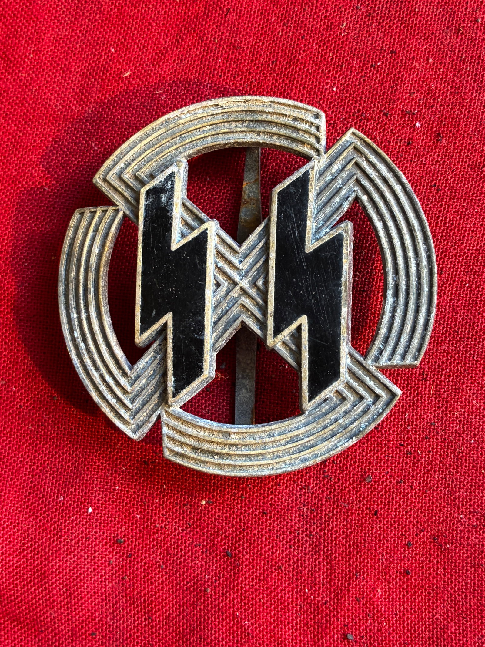 WWII GERMAN WAFFEN SS LEISTUNG BADGE BY RZM M1/25: WWII German Waffen-SS Leistung badge. Black enamel SS runes attached by folded pins to a ribbed sunwheel swastika. Flat vertical pin with 'c' catch. Very good condition. 2 inch diameter. Maker marked 