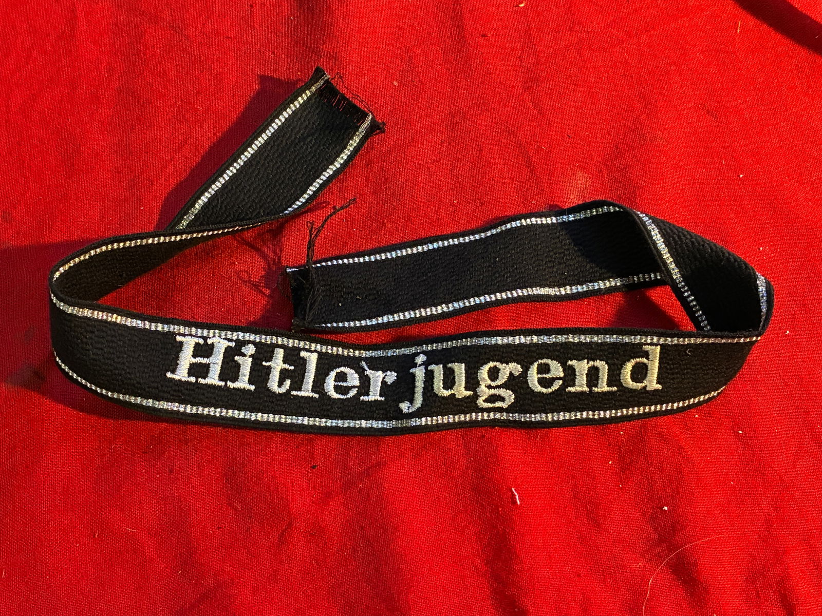 WWII GERMAN WAFFEN SS HJ HITLER YOUTH CUFF TITLE: WWII GERMAN WAFFEN SS HJ HITLER YOUTH CUFF TITLE. The front reads Hitlerjugend. Has six flat silver bullion wire strands along the top and bottom borders. Machine embroidered cotton thread on a black