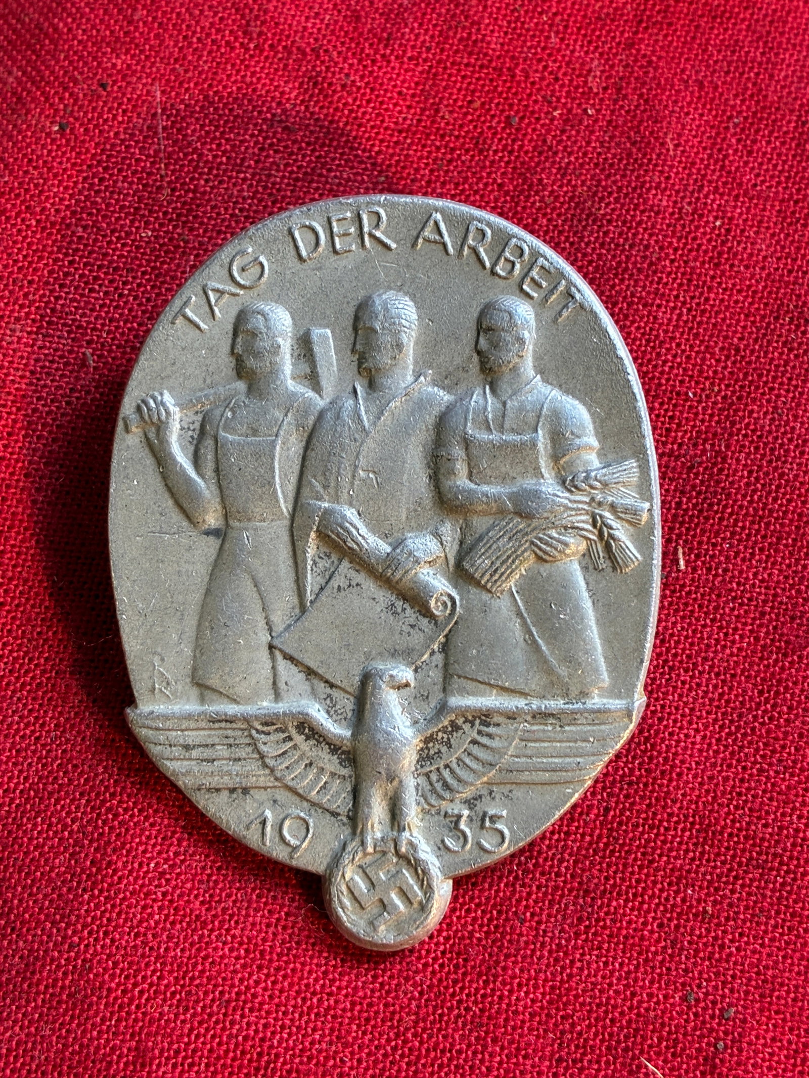 WW2 German Labour Day 1935 Badge, (Tag Der Arbeit): WW2 German Labour Day 1935 Badge, (Tag Der Arbeit). An aluminium grade light weight constructed example. Displaying three individual trade figures with words “TAG DER ARBEIT” above. Beneath th