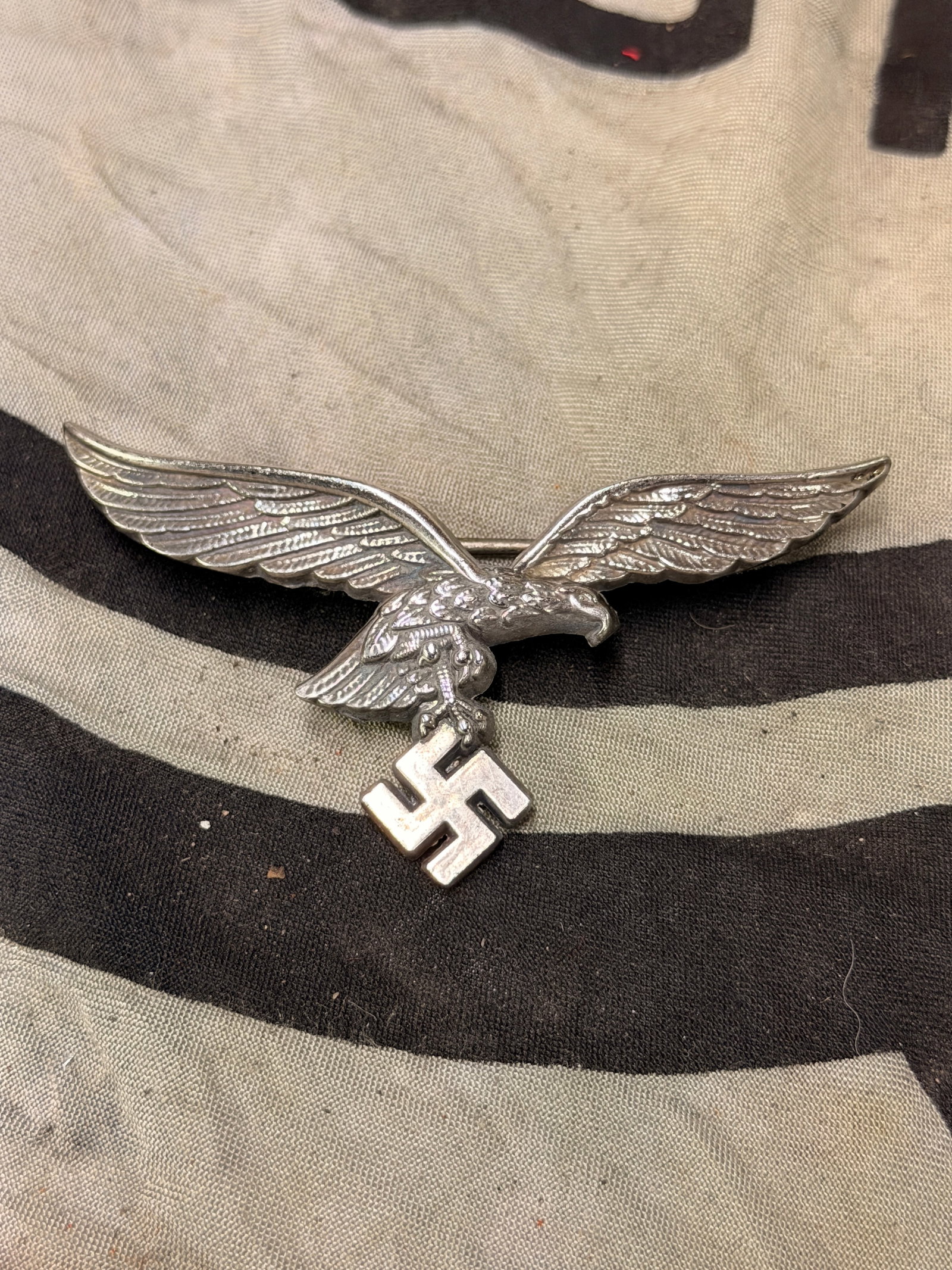 WWII LUFTWAFFE OFFICER SUMMER TUNIC DETACHABLE BREAST EAGLE BY ASSMANN: WWII GEMAN LUFTWAFFE OFFICER SUMMER TUNIC DETACHABLE BREAST EAGLE. GOOD PIN BACK WITH HOOK CATCH. MAKER MARKED A FOR ASSMANN. MEASURES SLIGHTLY OVER 3 1/4? FROM WING TIP TO WING TIP. SHOWS AVERAGE USE