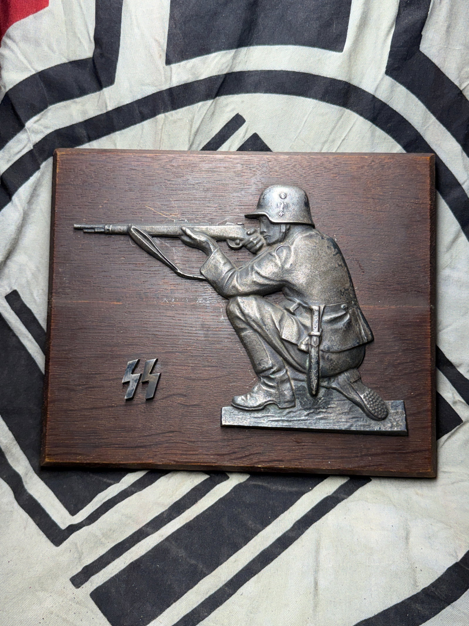 VET BRING BACK WW2 GERMAN WAFFEN SS OFFICER WALL PLAQUE: VET BRING BACK WW2 GERMAN WAFFEN SS OFFICER WALL PLAQUE. A VERY RARE EXAMPLE. SHOWS AN SS SOLDIER WITH RIFLE AIMING/SHOOTING. HAS THE SS INSIGNIA ON IT AS WELL. PLEASE VIEW ALL DETAILED PICTURES. A VE