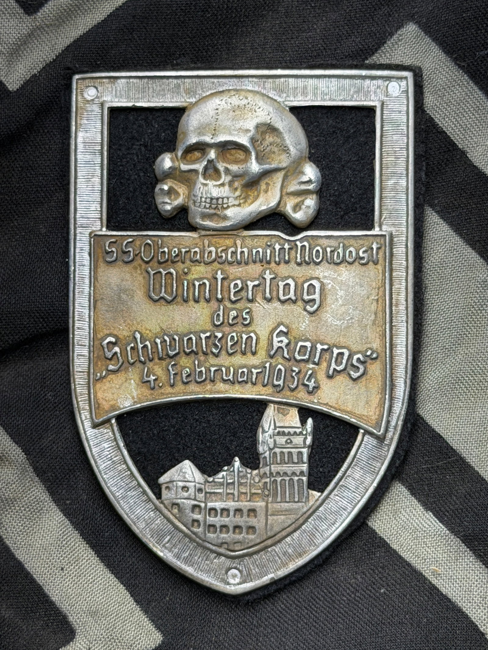 WWII GERMAN WAFFEN SS 1934 WINTERTAG BADGE BY RZM: WWII GERMAN WAFFEN SS 1934 WINTERTAG BADGE BY RZM. German WWII Waffen SS 1934 Wintertag Badge. Measures 2 3/16 inches wide by 3 3/16 inches tall. The front shows a Waffen SS skull at the top with a ca