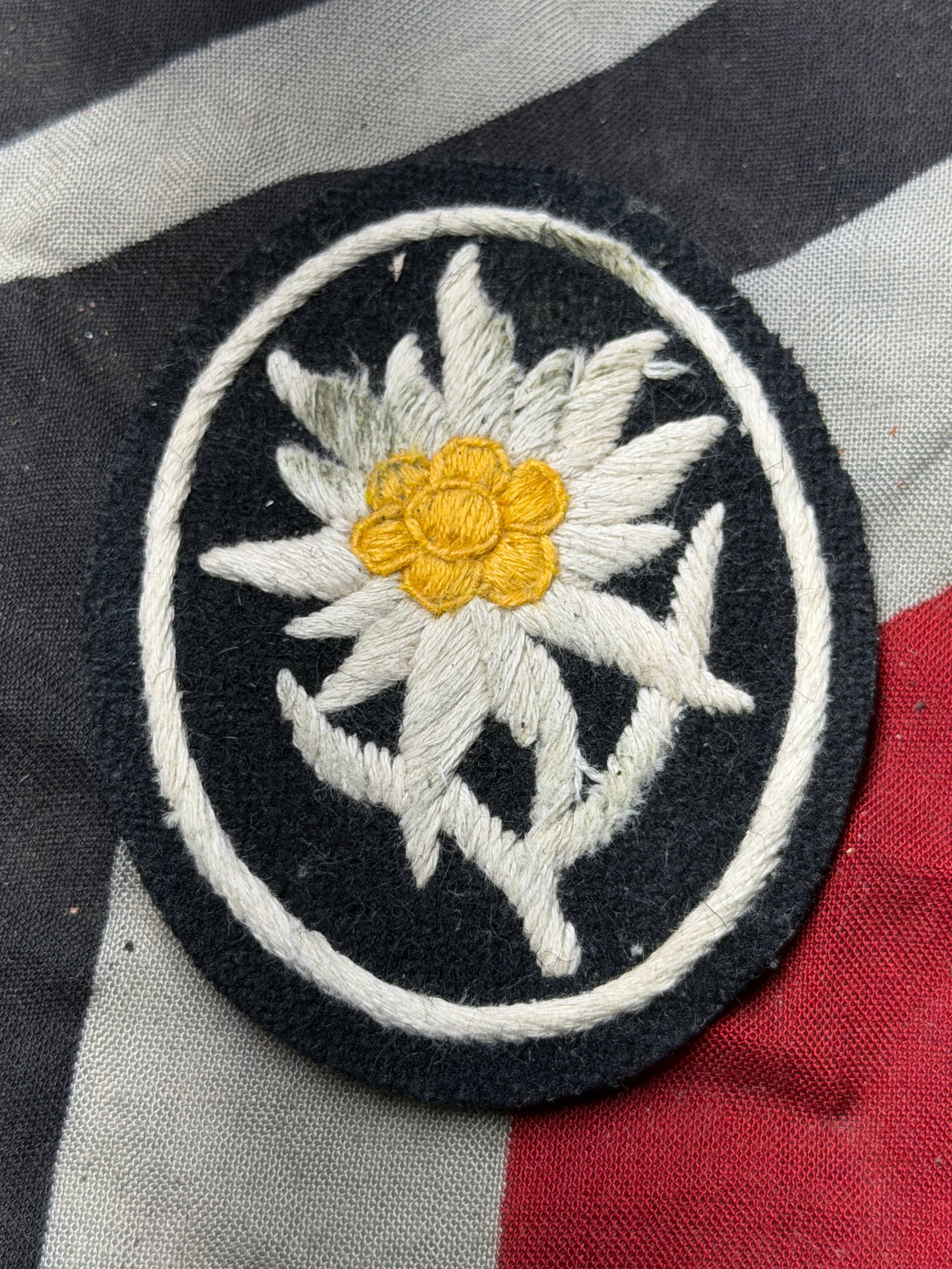 WW2 GERMAN WAFFEN-SS GEBIRGSTRUPPEN SLEEVE EDELWEISS PATCH: WW2 GERMAN WAFFEN-SS GEBIRGSTRUPPEN SLEEVE EDELWEISS PATCH. A Waffen-SS Gebirgstruppen Sleeve Edelweiss Patch, embroidered in silver-grey flower petals, leaves, and stem; with yellow stamen; on black 