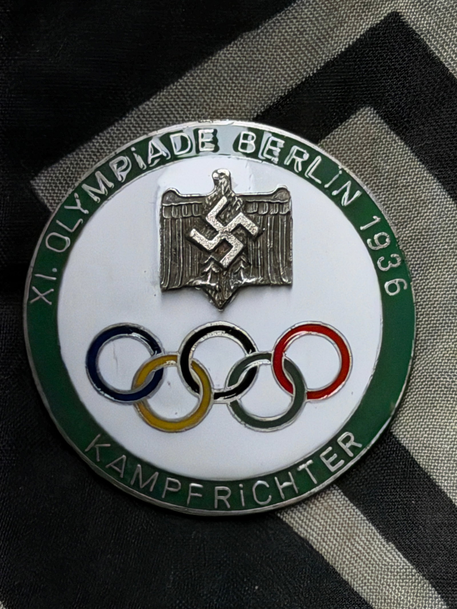 A 1936 WW2 GERMAN BERLIN OLYMPIC KAMPFRICHTER BADGE BY GES. GESCH.: A German Berlin 1936 Olympic Games Richter Kampfrichter badge. The badge obverse with a Nazi swastika rune is enameled in white color, with five Olympic rings and a green enameled border with an inscr