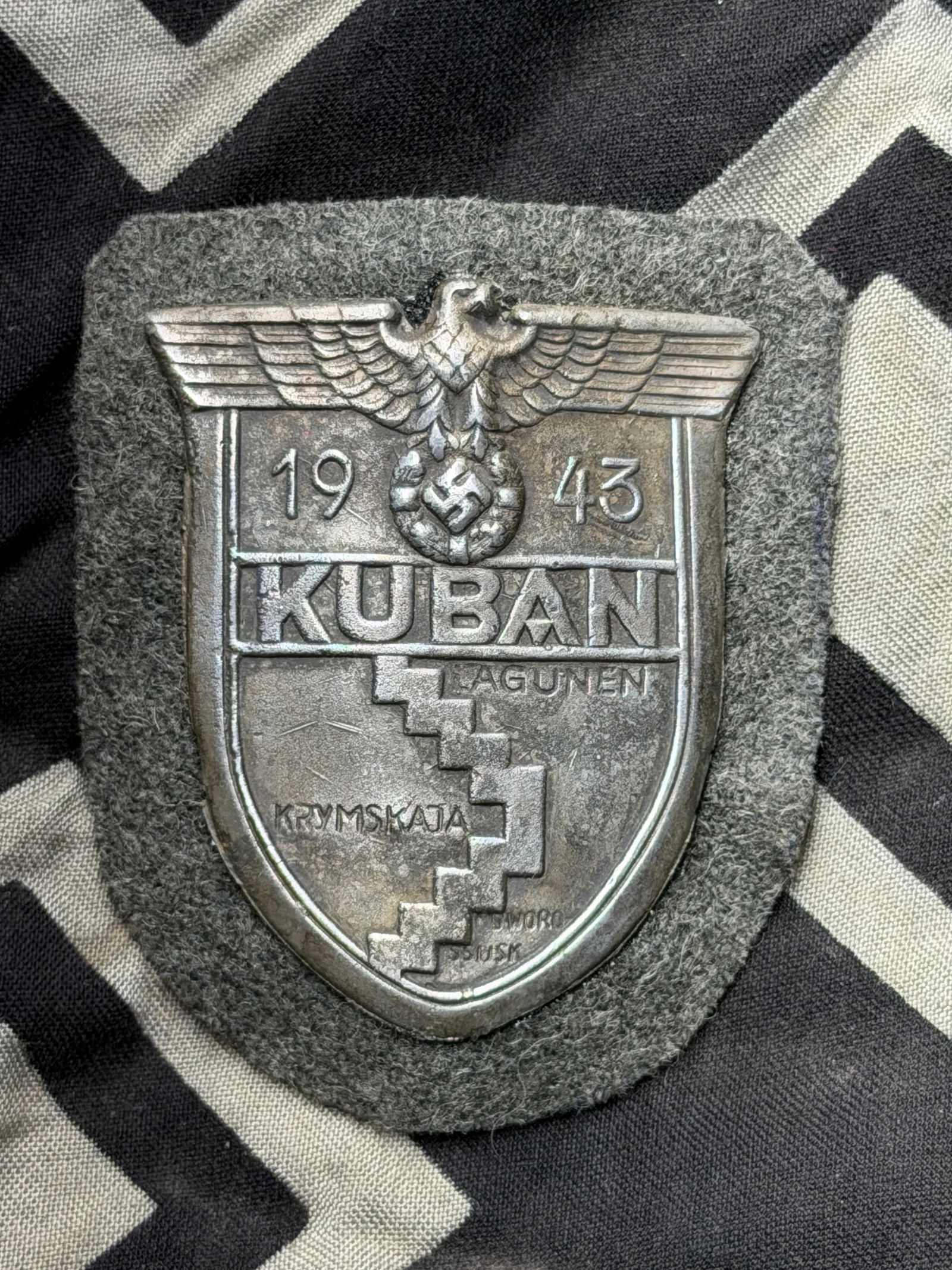 WW2 German Kuban Campaign Shield Army By FAB: WW2 German Army Kuban Campaign Shield By FAB. Steel based die stamped shield with bronze wash and backing plate with Army wool cloth. All four tabs appear to be present on back under the paper backing