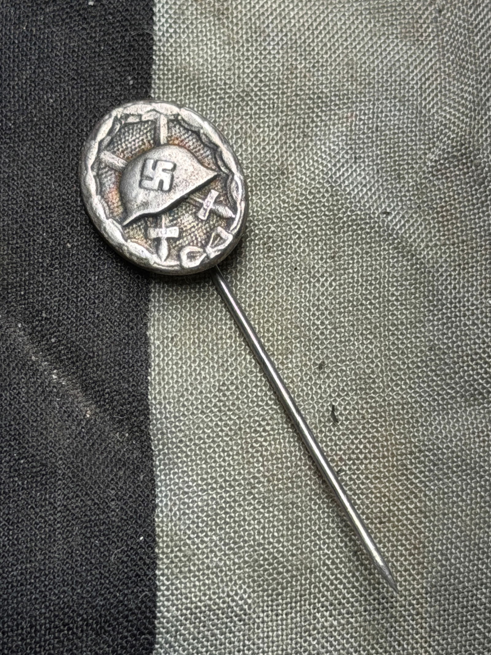 World War II-era German Wound Badge stickpin Silver Grade (2nd Class) version: World War II-era German Wound Badge stickpin Silver Grade (2nd Class) version. Front design: Features a German-style helmet (Stahlhelm) bearing a swastika, over two crossed swords within an oval wreat