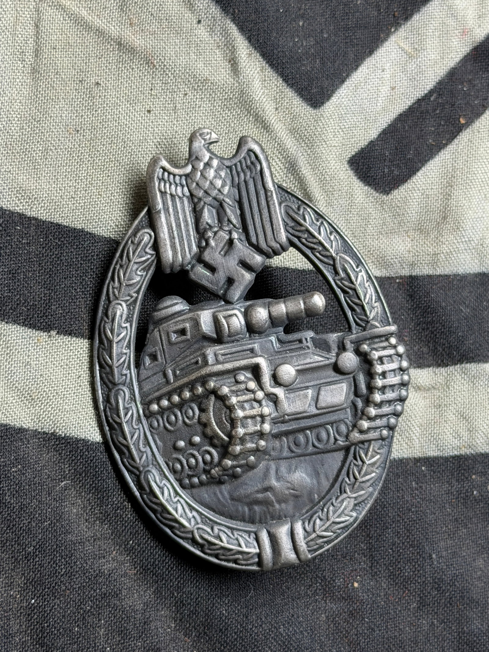 WWII German Panzer Assault Badge (Panzerkampfabzeichen): WWII German Panzer Assault Badge (Panzerkampfabzeichen). he badge is oval-shaped, featuring a German Panzer tank moving left within a laurel wreath. At the top is the German eagle clutching a swastika