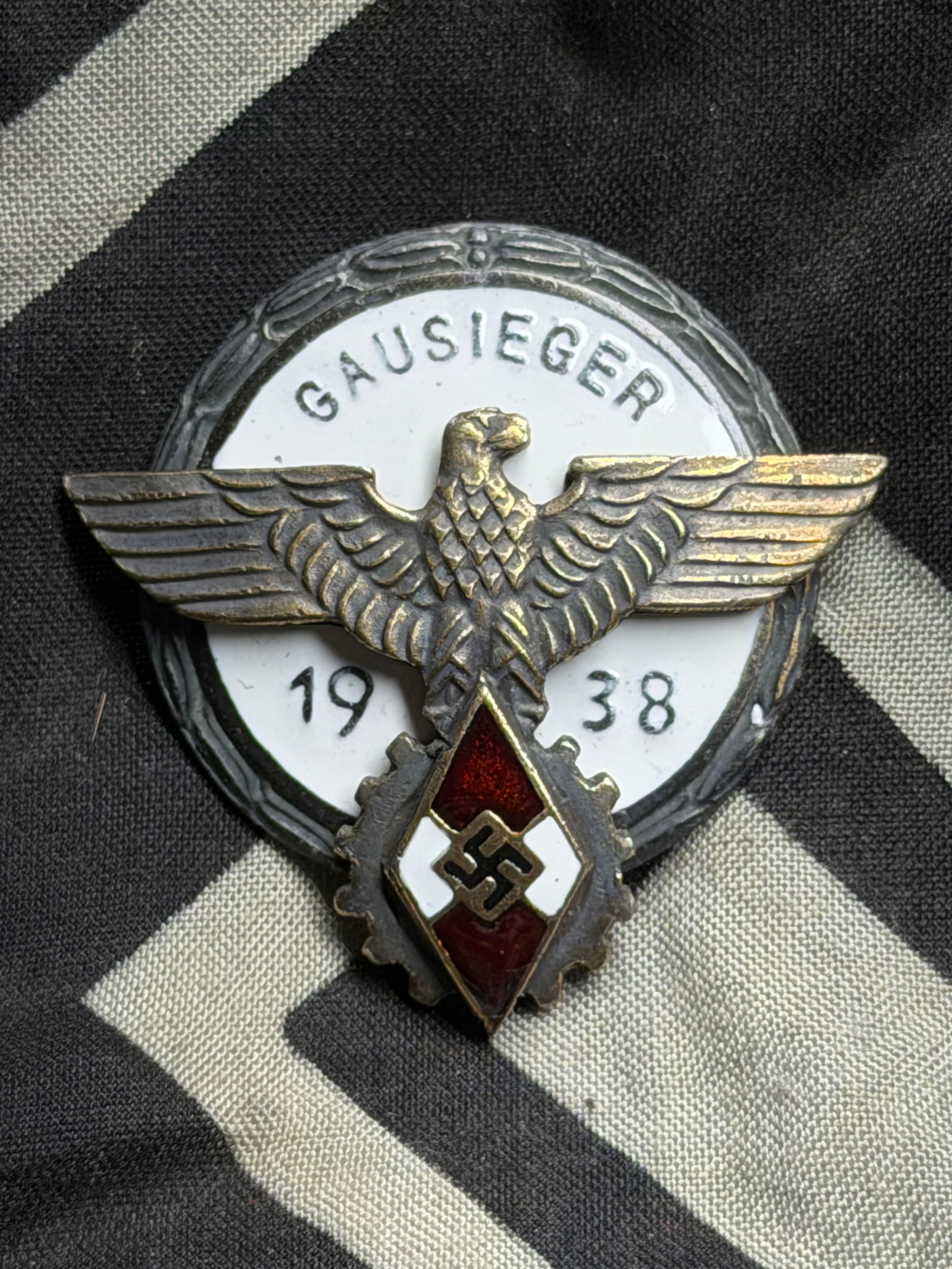 WW2 German HJ Gausieger Badge By Gustav Brehmer: WW2 German HJ Gausieger Badge By Gustav Brehmer. A scarce HJ Gausieger Badge by Gustav Brehmer, multi-piece construction silvered tombac and enamel. The obverse of the badge depicts a circular oak lea