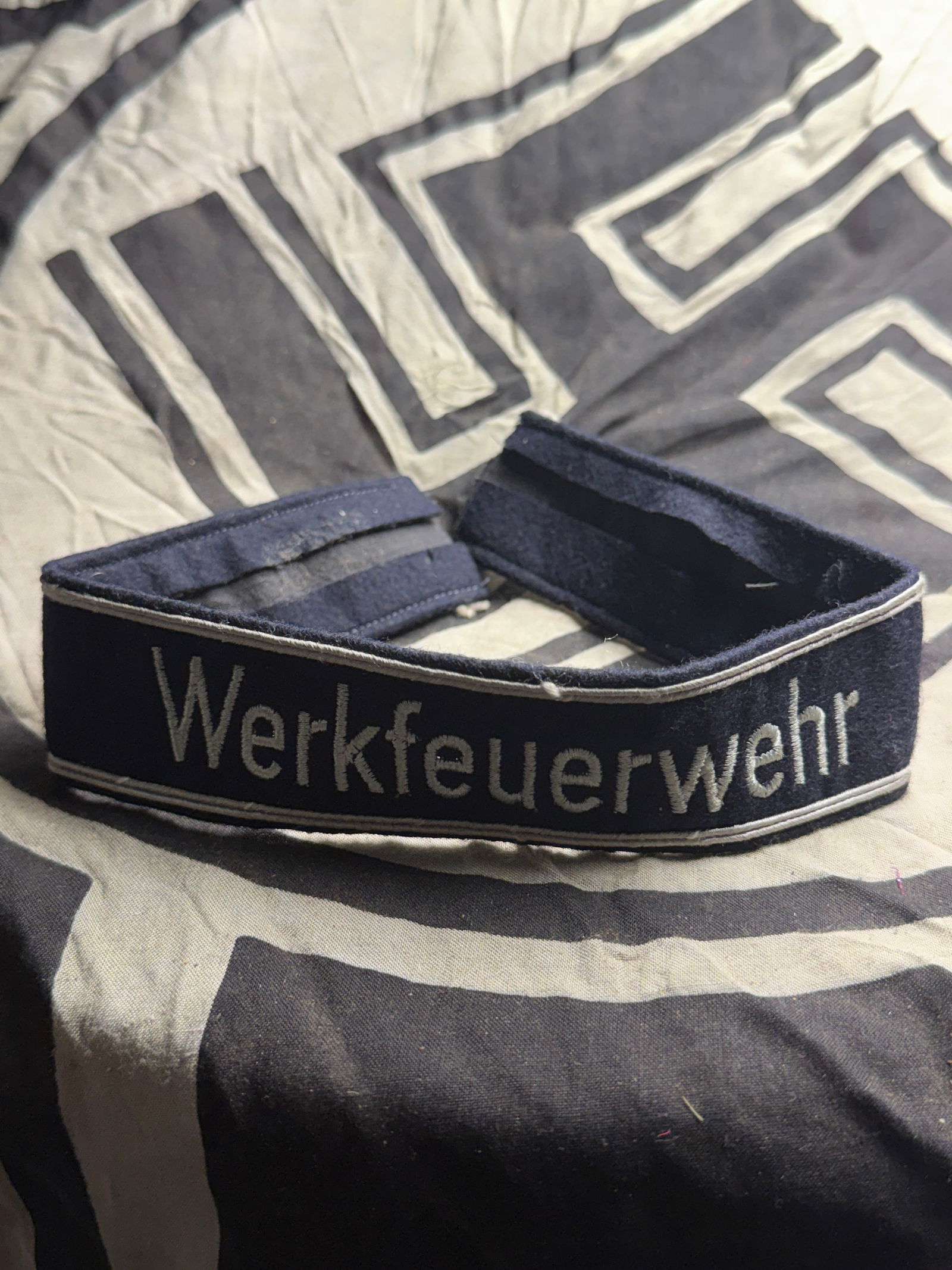 WW2 German “Werkfeuerwehr?? Factory Fire Brigade cuff title: WW2 German “Werkfeuerwehr” Factory Fire Brigade cuff title. Dark navy blue wool base with silver-grey embroidered text “Werkfeuerwehr.” White/silver piping along the top and bottom edg
