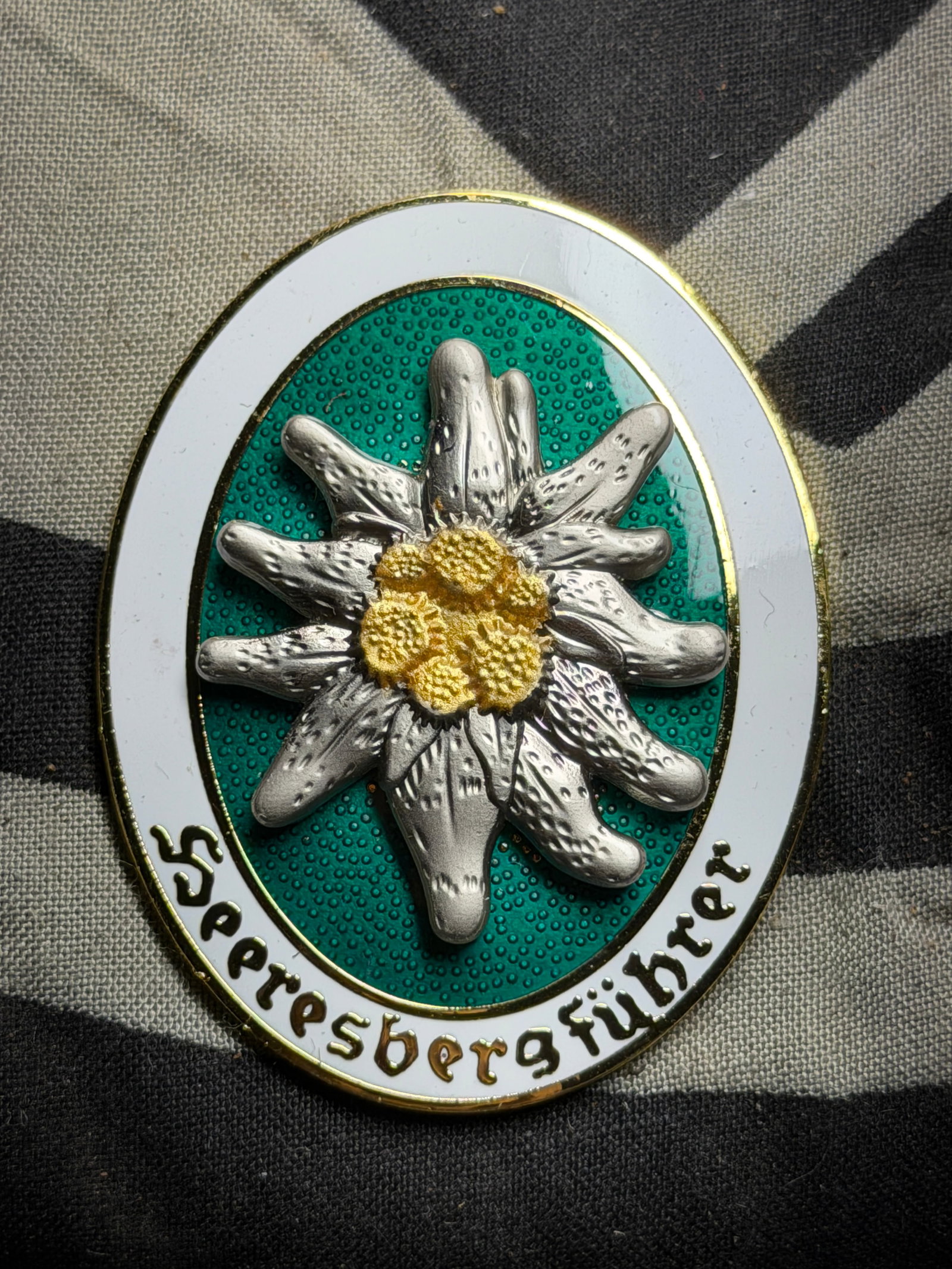 WW2 German Mountain Division Edelweiss Enameled Badge By Deschler & Sohn Munchen: WW2 German Mountain Division Edelweiss Enameled Badge By Deschler & Sohn Munchen. A rare find. Shows good wear and use with a beautiful overall patina. Please view all detailed pictures. A rare exampl