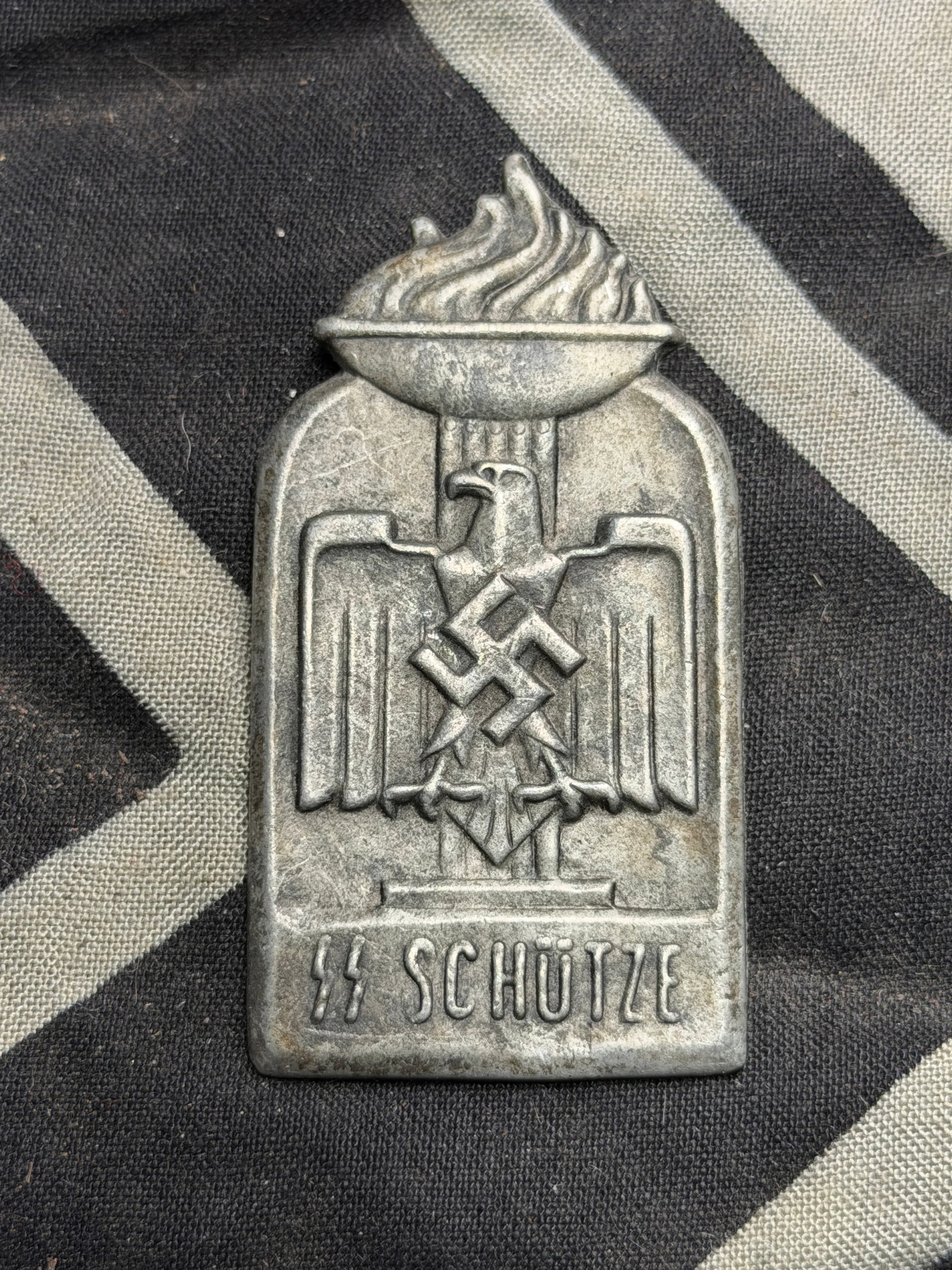 WW2 GERMAN WAFFEN-SS SCHUTZE RALLY BADGE MARKED REICH: WW2 GERMAN WAFFEN-SS SCHUTZE RALLY BADGE MARKED REICH. Waffen-SS Schutze Rally Badge, metal example showing a Sports Association style eagle set upon flaming torch with SS runes and Schutze underneath