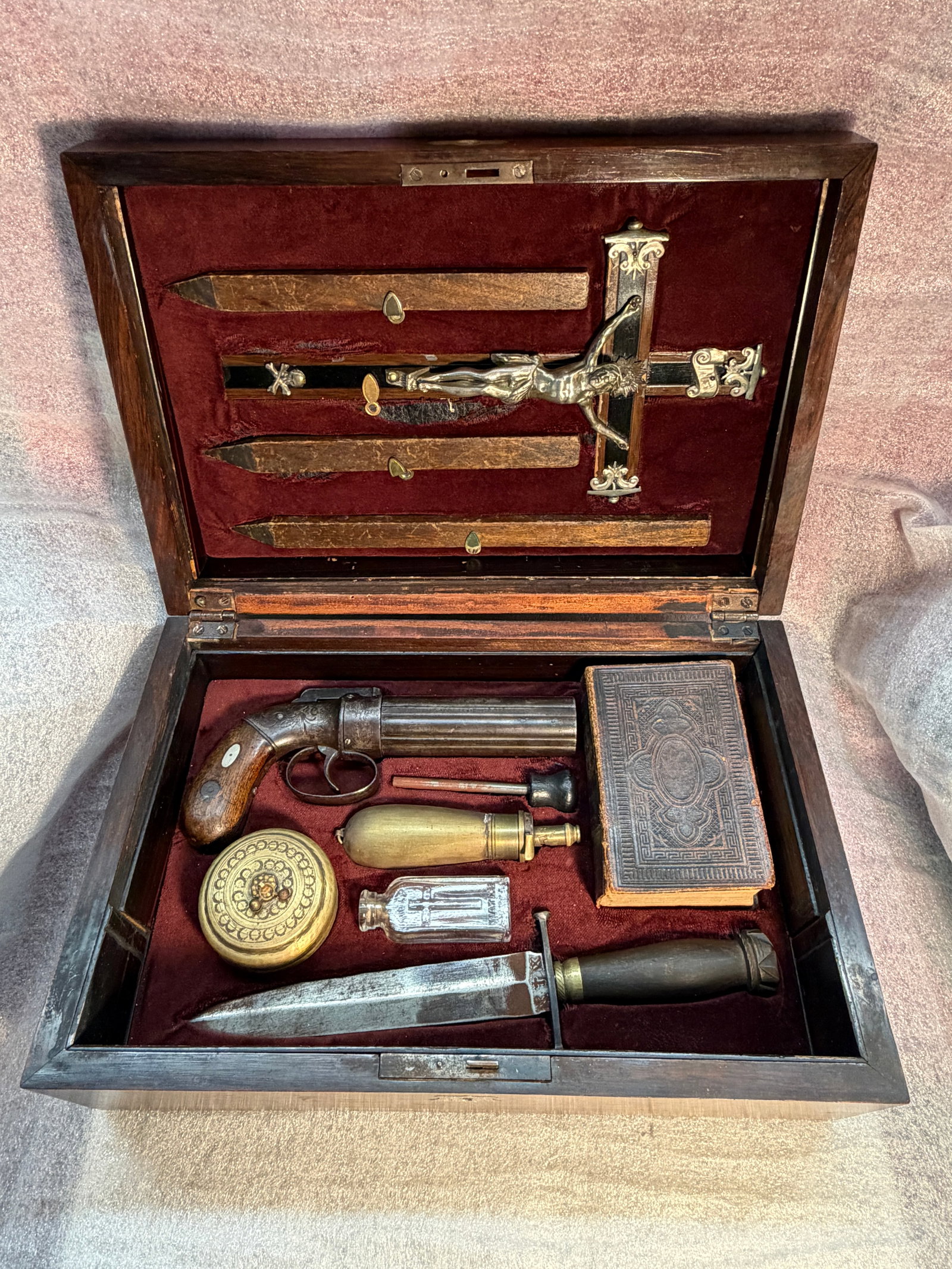 C. 1850'S Vampire Hunting Kit, Continental Europe or England: A finely crafted 19th-century cased “vampire hunting kit,” housed in a veneered mahogany box with brass and mother-of-pearl inlay, lined in crimson velvet. The fitted interior contains a colle