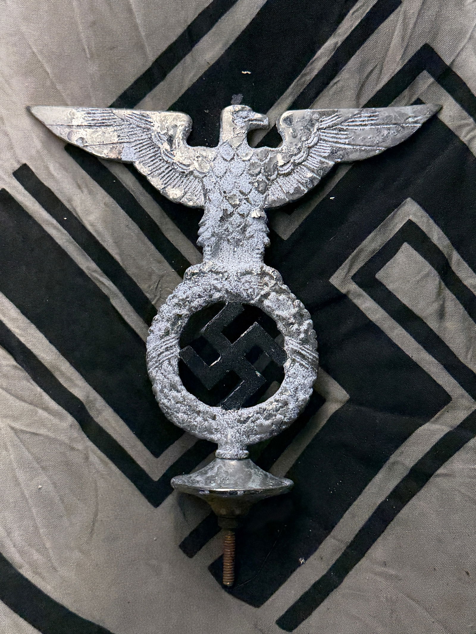 WW2 German Vehicle Hood Ornament — Reichsadler Emblem (circa 1936–1945): This cast-metal hood ornament features the Reichsadler (Imperial Eagle) — a stylized eagle clutching a wreath enclosing a swastika, the central symbol of Nazi Germany. This emblem was prominently us