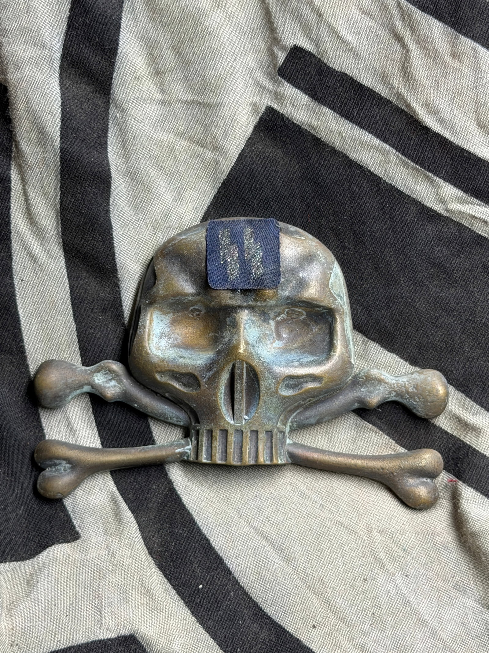 WW2 German SS Totenkopf (Death’s Head) Emblem — Waffen-SS: his artifact depicts the Totenkopf, or “Death’s Head,” a prominent emblem of the Schutzstaffel (SS) and its elite Waffen-SS units during the Second World War. The design features a stylized 