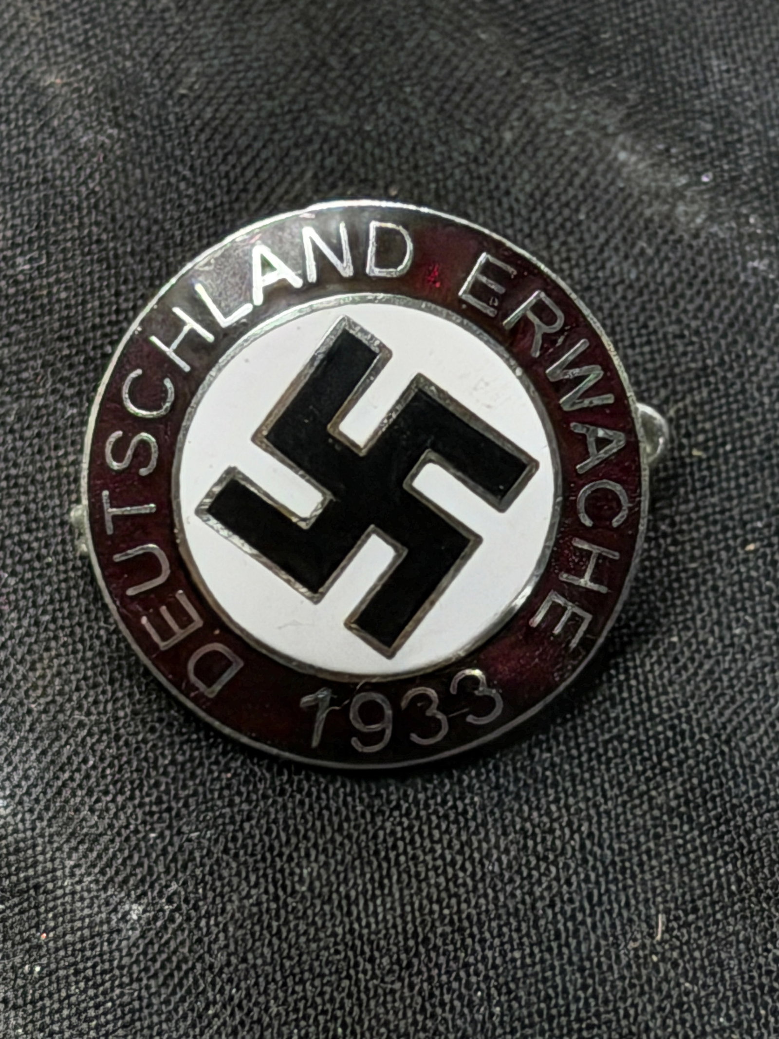 WW2 German Deutschland Erwache Commemorative Party Badge By RZM M1/129: WW2 German Deutschland Erwache Commemorative Party Badge By RZM M1/129. This circular enameled badge, approximately 3 cm in diameter, features a black symbol set within a white field surrounded by a d