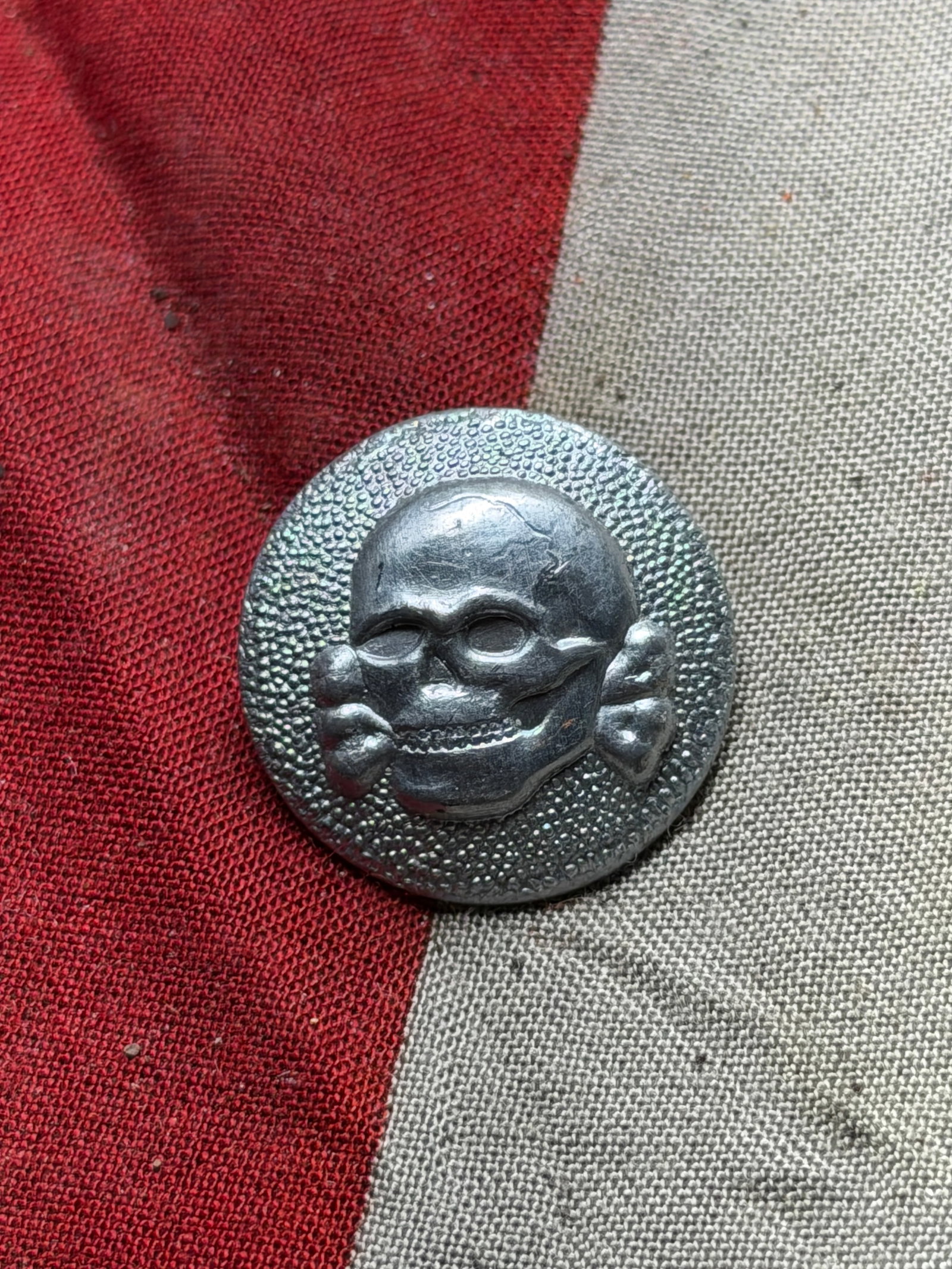 Totenkopf (Death’s Head) Cap Button WW2 Germany, SS Insignia, circa 1940: This metallic button, featuring a skull and crossbones motif known as the Totenkopf, was used by the Schutzstaffel (SS) during Nazi Germany’s regime (1933–1945). The Totenkopf symbol, historically