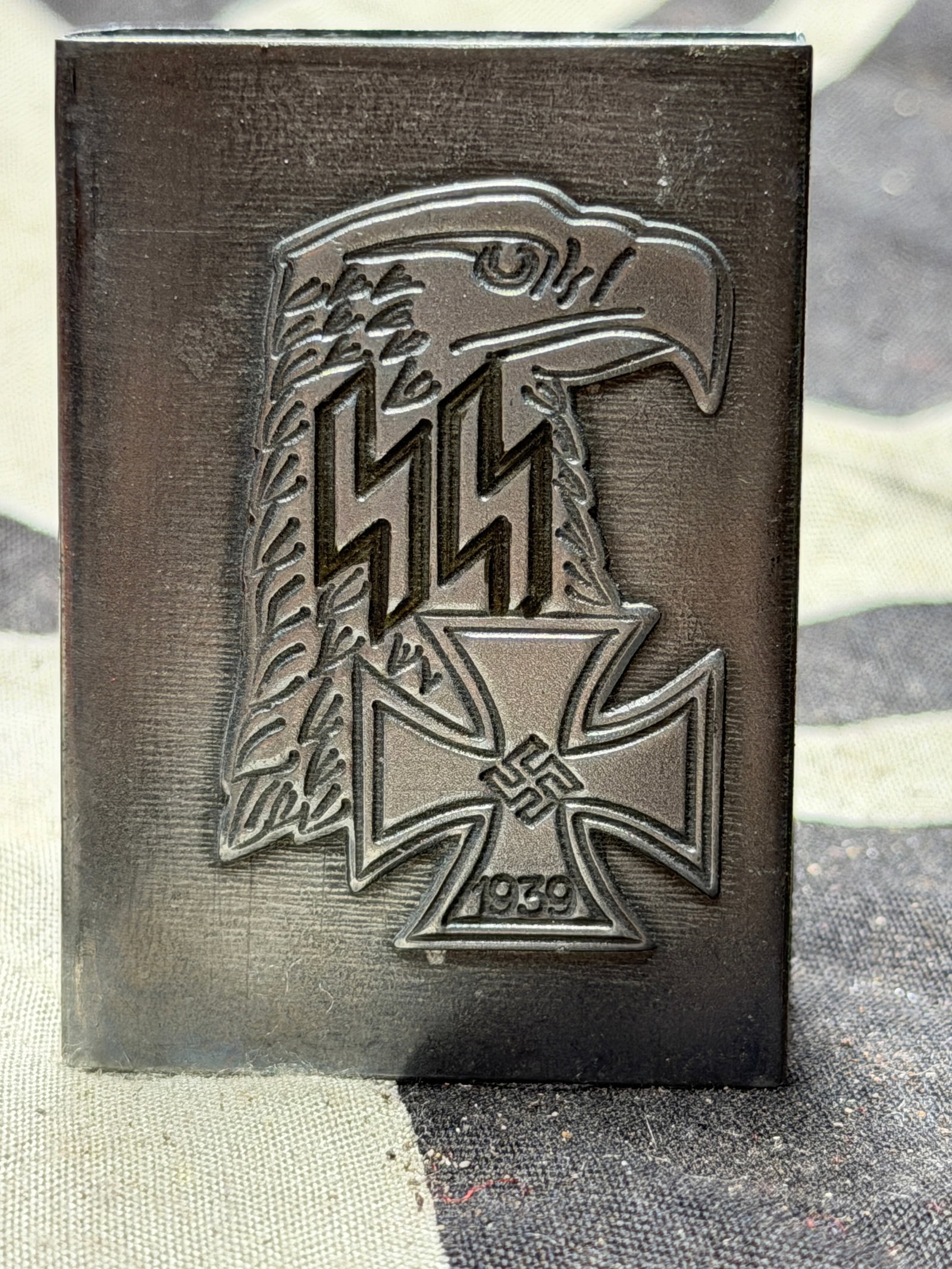 WW2 German SS Commemorative Cigarette Case – Waffen-SS and Iron Cross Motif, 1939: This metal cigarette case features an embossed design combining two of Nazi Germany’s most notorious symbols: the SS double lightning-bolt runes overlaid on an eagle’s profile, and the 1939 Iron C