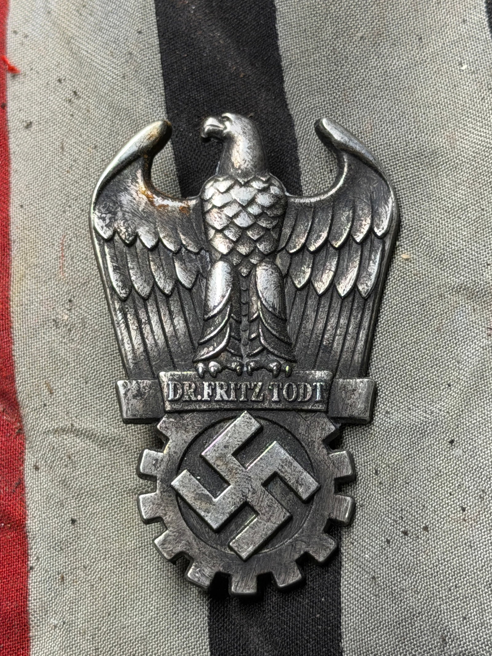 Organization Todt Commemorative Badge, WW2 Germany, circa early 1940s: This metal badge features an eagle grasping a cogwheel enclosing a swastika, with the inscription “Dr. Fritz Todt” across the center bar. The reverse includes a simple pin-back fastener. Measu