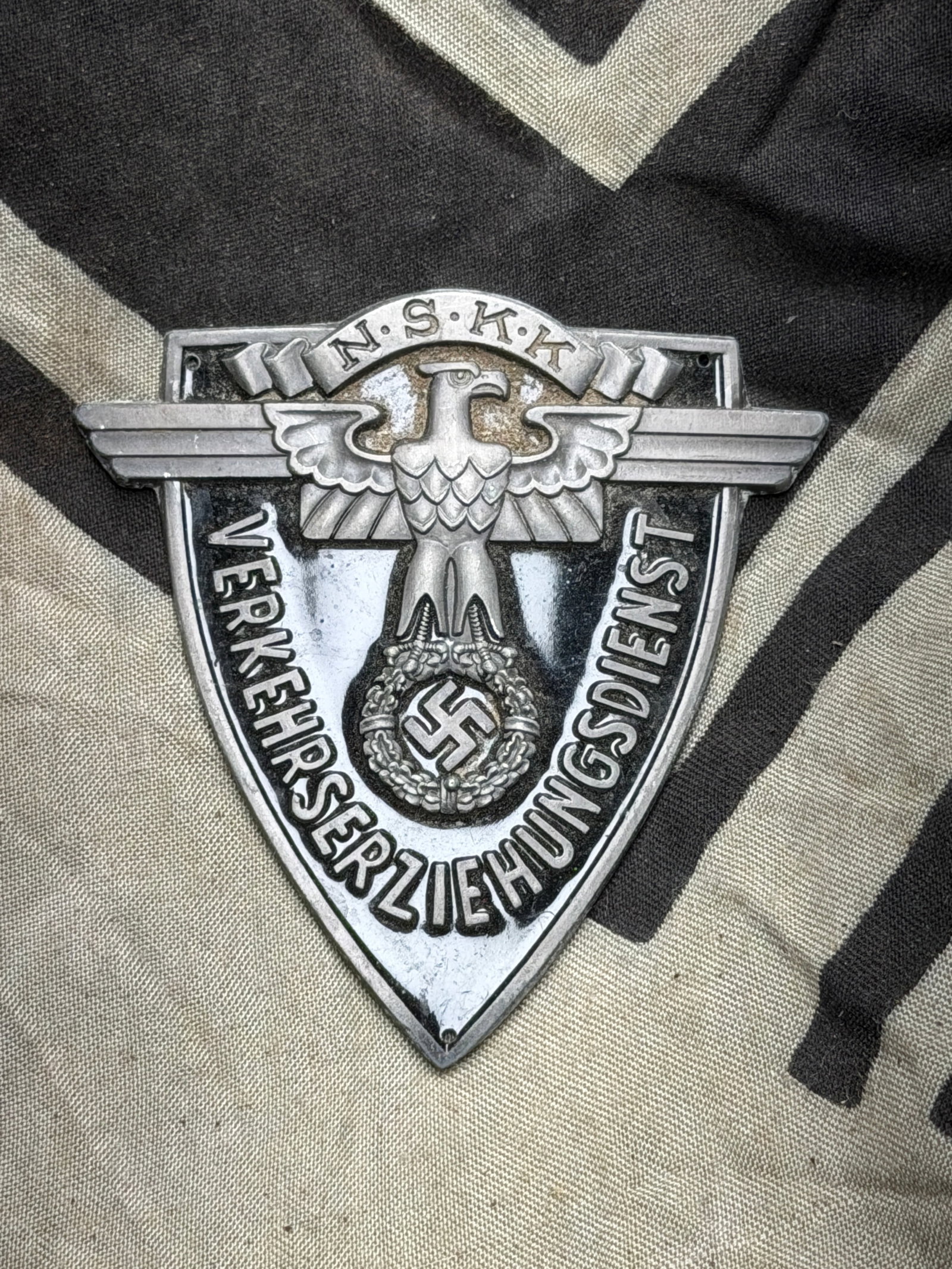 NSKK “Verkehrserziehungsdienst?? Plaque (National Socialist Motor Corps), WW2 Germany, circa: This metal shield-shaped plaque bears the emblem of the Nationalsozialistisches Kraftfahrkorps (NSKK), or National Socialist Motor Corps. The design features a spread-winged eagle clutching a wreath e