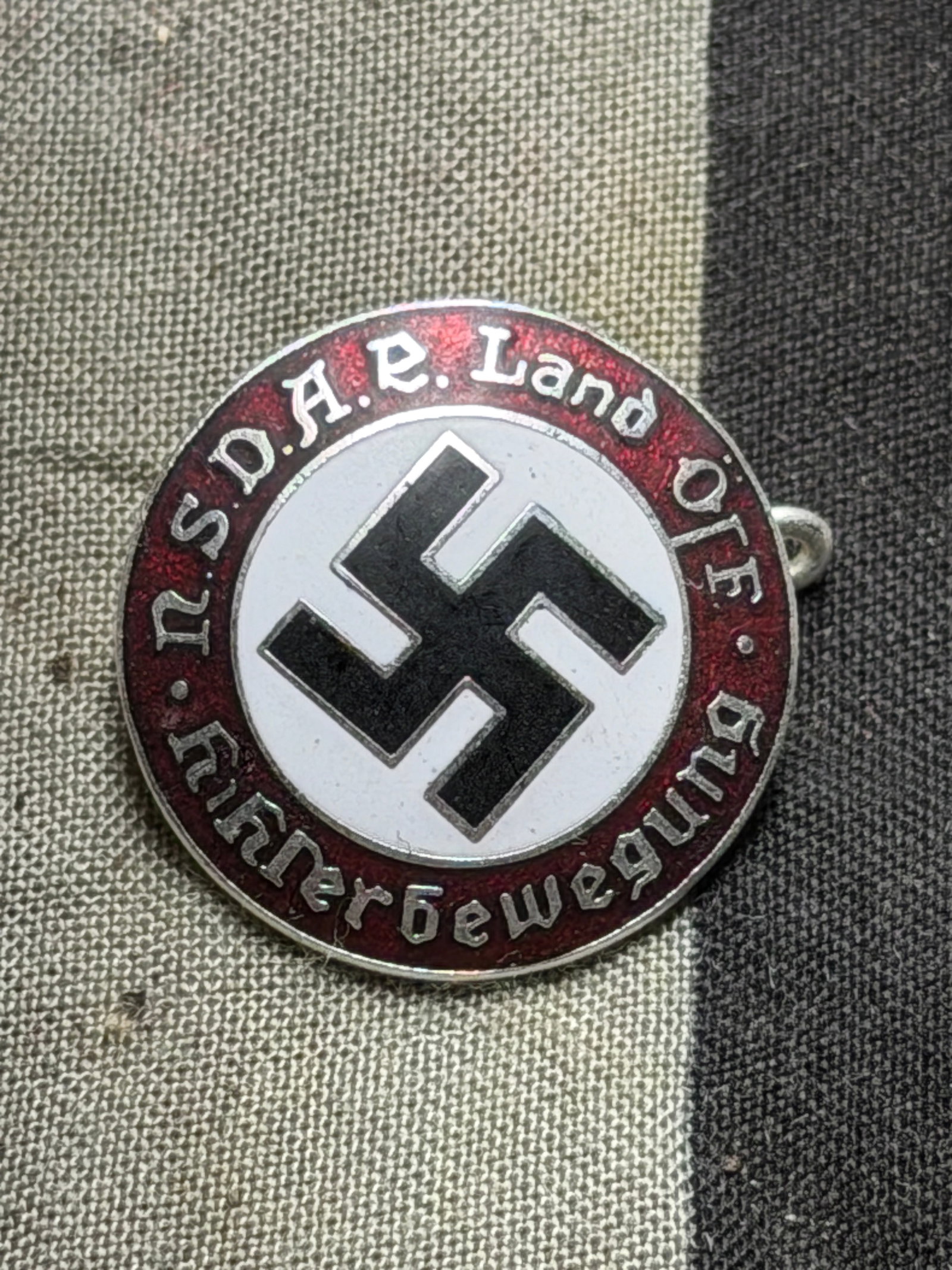 Nazi Party Regional Membership Badge (NSDAP Land O.F. Männerbewegung), WW2 Germany, circa: This circular enamel badge bears the black swastika emblem in the center on a white field, surrounded by a red border with the inscription “N.S.D.A.P. Land O.F. Männerbewegung” (National Soci