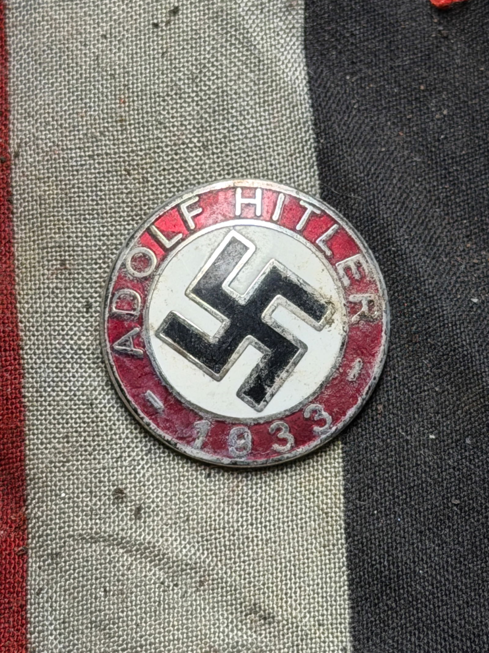WW2 German Commemorative Political Badge – “Adolf Hitler 1933?? Lapel Enameled Pin By RZM: This circular metal badge dates from around 1933, commemorating the year Adolf Hitler was appointed Chancellor of Germany. The front design features a red and white enamel face with a black swastika a