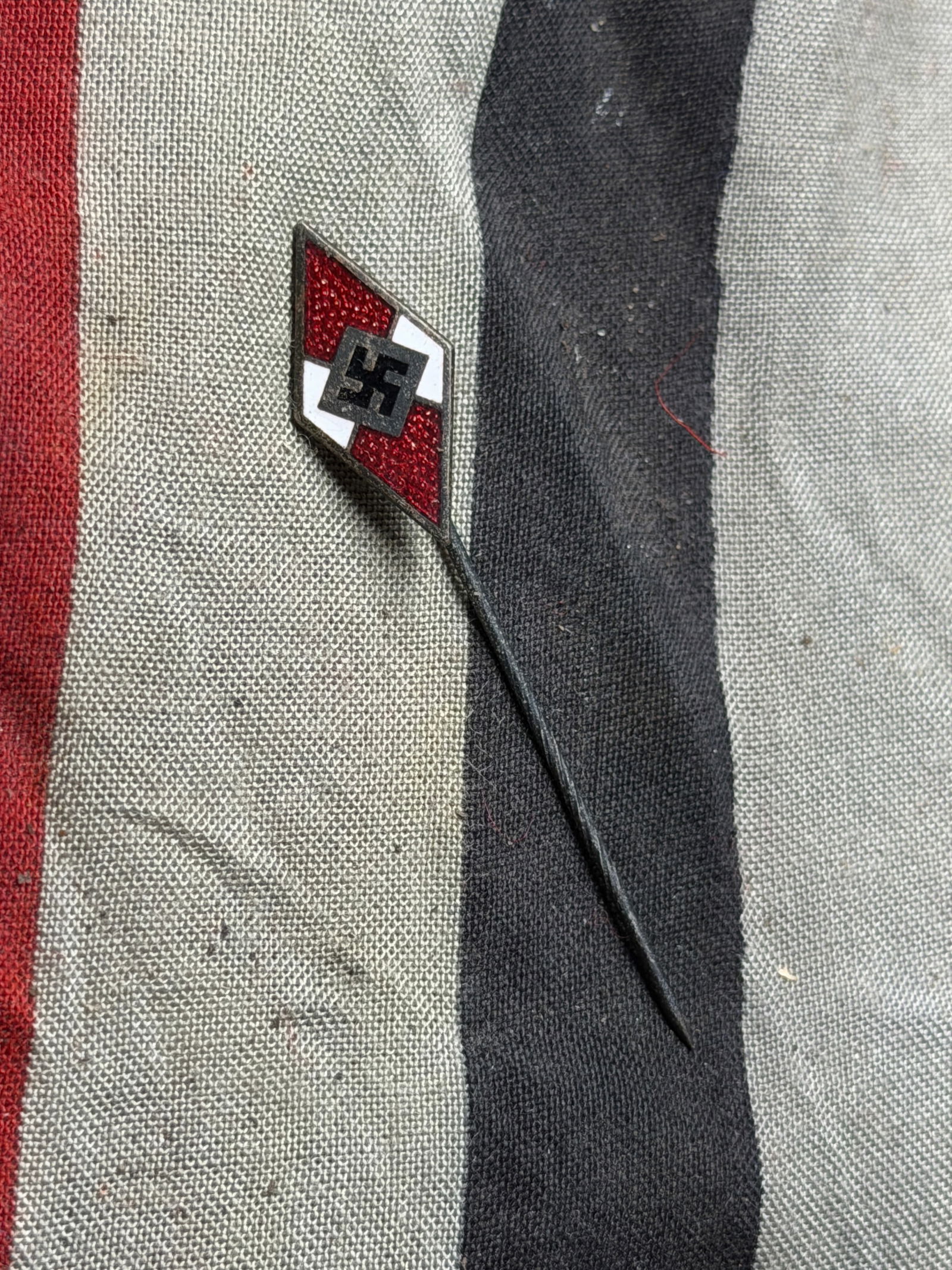 WW2 German Youth Organization Stickpin with Diamond Emblem: This artifact is a metal and enamel stickpin featuring a red, white, and black diamond-shaped design, mounted on a slender pin. The motif, characterized by a geometric red diamond divided by a white l