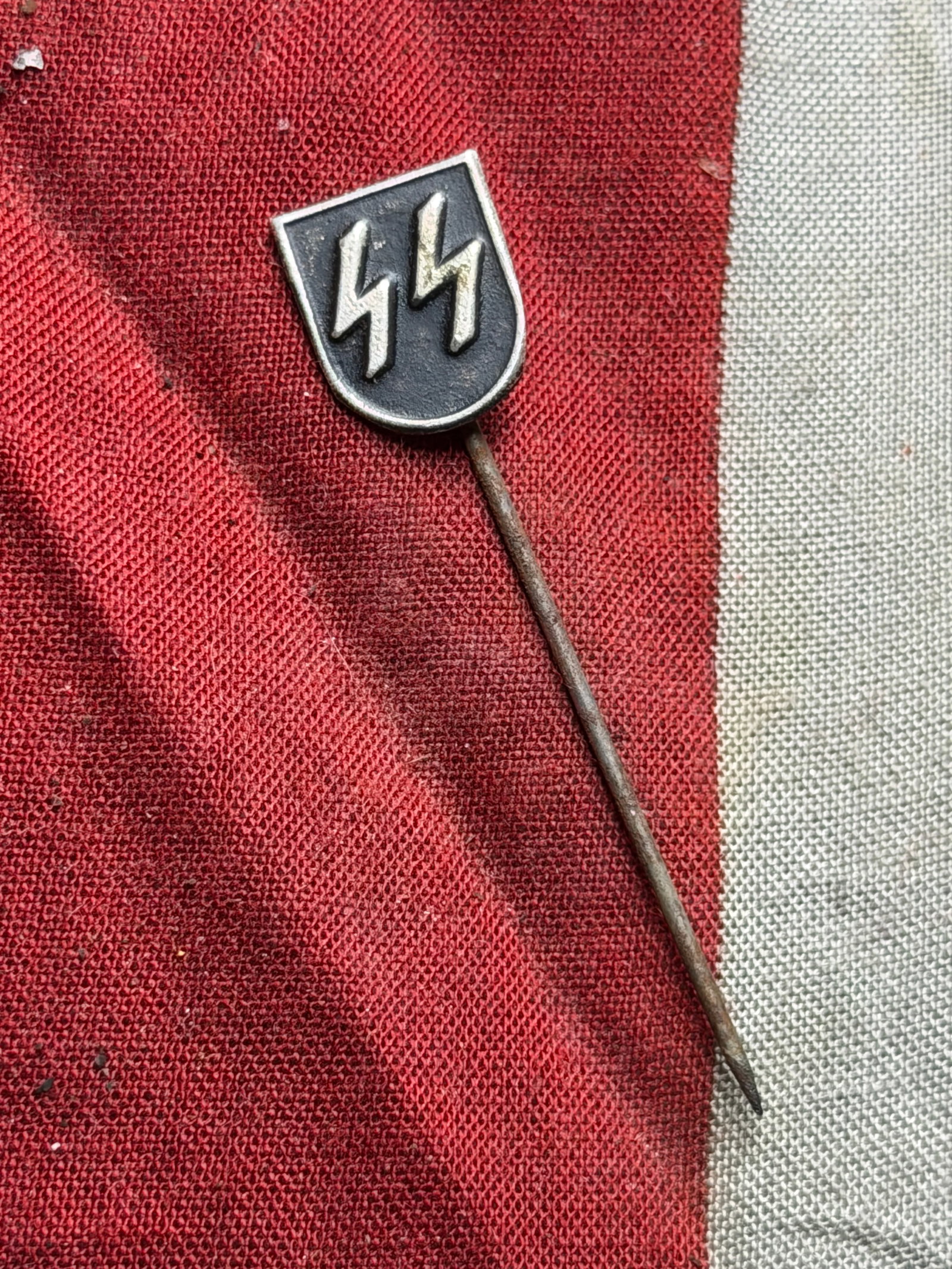 WW2 German Schutzstaffel (SS) Membership Lapel Pin — Stickpin Type: This small metal stickpin bears the SS double-lightning bolt emblem within a black enamel shield. The reverse side shows no visible maker’s mark, and the pin is a simple single-prong design. The ent